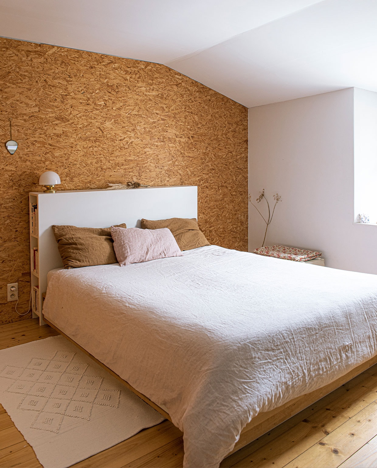 Hoofdeinde bed gemaakt door Kevin, linnen kussenhoezen en dekbedovertrek By Mölle, muur afgetimmerd met OSB-plaat, karpet uit Portugal, vintage spiegel, vloer van grenen planken.
