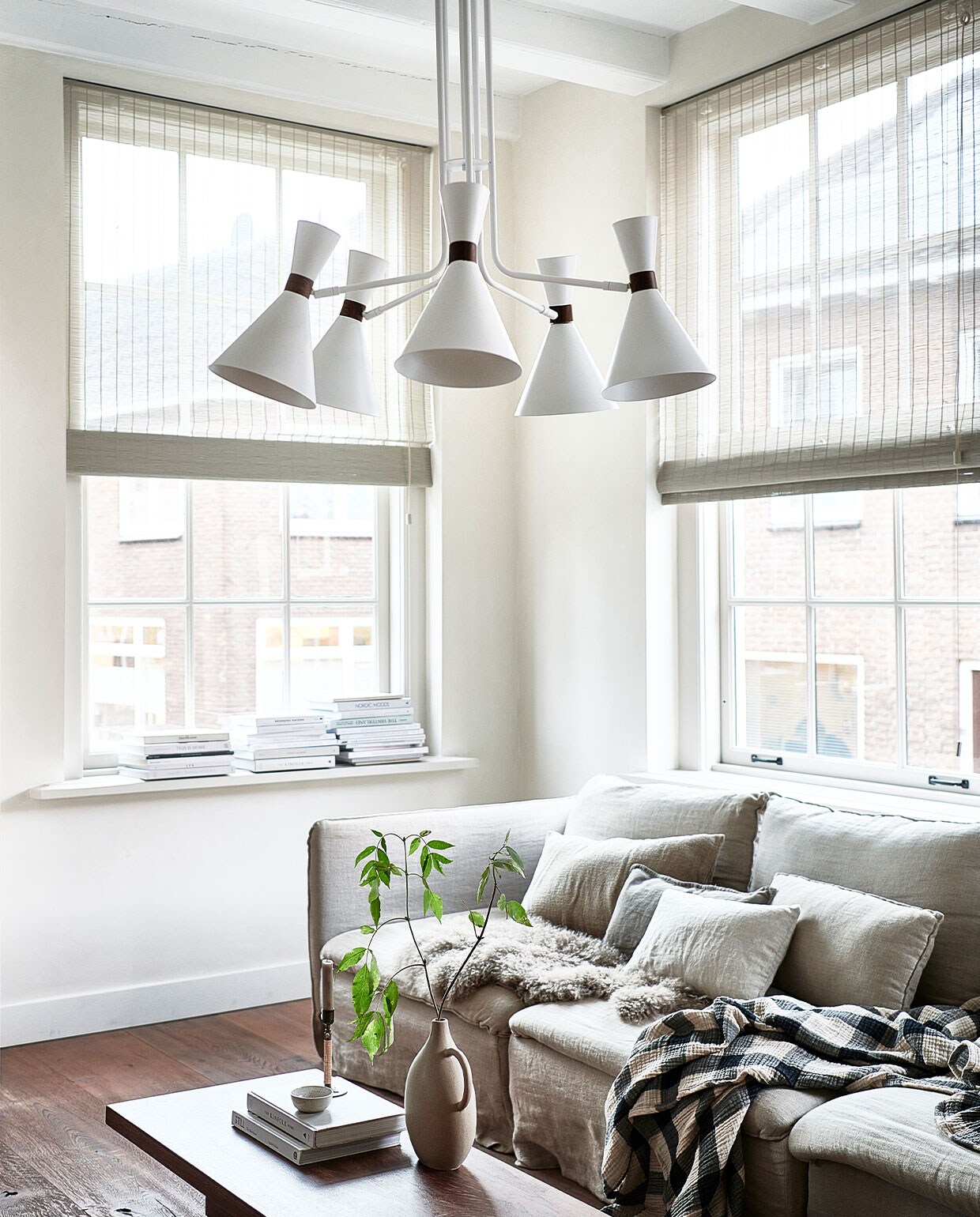 Matte zandgrijze metalen hanglamp Hoodies (5 lampen), 20x86x83,5 cm € 399,- (ook verkrijgbaar in matzwart) | M.m.v. ikea.nl (bank Söderhamn), bemz.com (linnen hoes voor de bank), zarahome.com (vaas, kussens), hm.com (geblokt plaid), karwei.nl (schapenvacht), bauwerkcolour.com (muurverf kleur Mykonos), nature-deco.com (raamdecoratie). Overig privébezit.
