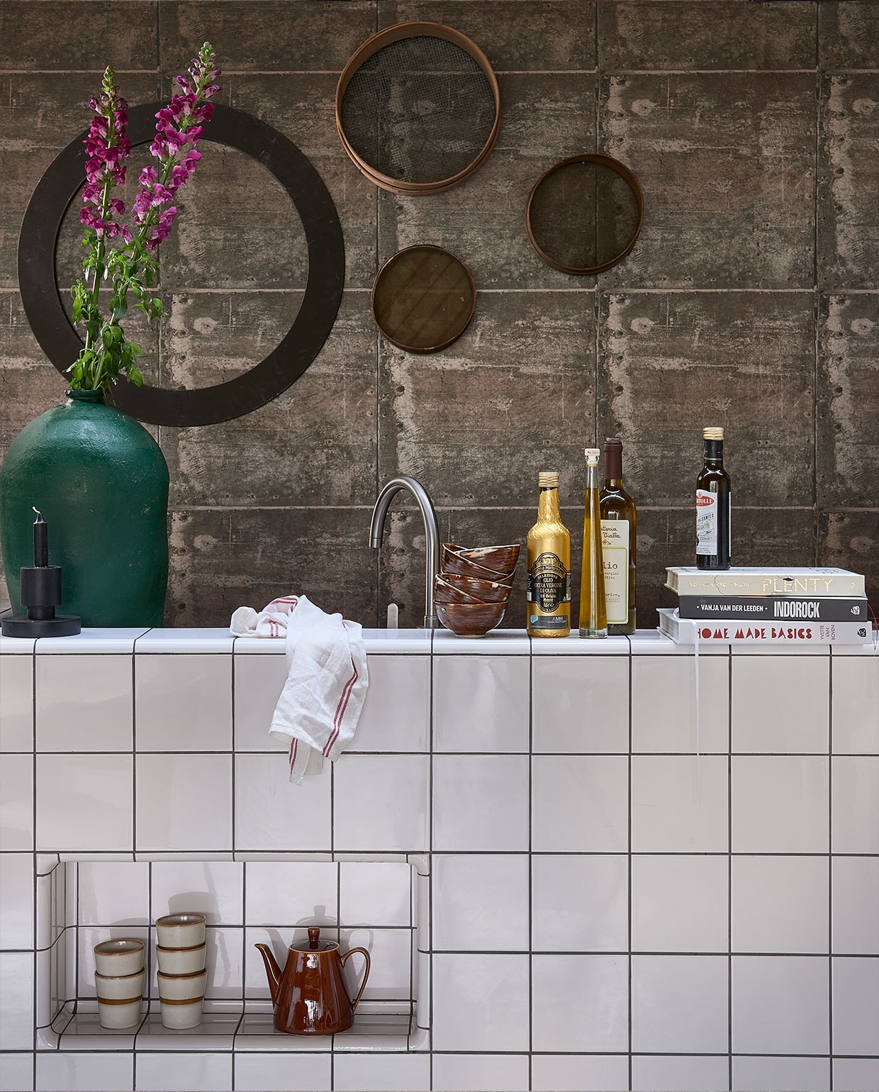 Behang met print van verweerde roestige metalen platen met klinknagels, 53 cm x 10,05 m, per rol € 49,50 (originwallcoverings). Hoge groene olijfpot € 140,-, zeven aan de wand vanaf € 15,- (vandijkenko). Bruine dessertschaaltjes, per stuk € 7,50, mok € 8,50 (hkliving). Glazendoek € 0,39 (ikea). Kandelaar zwart € 27,95 (fonq.be). Koffiepot privébezit.