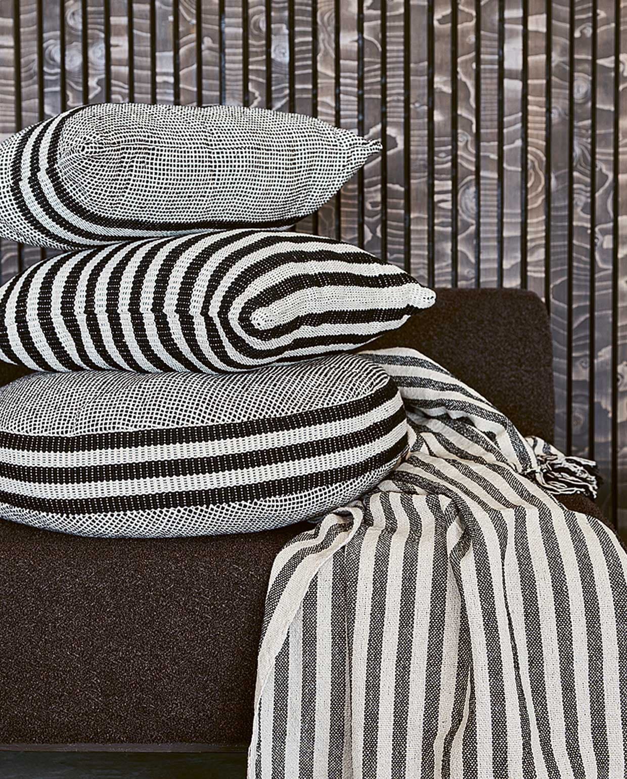 Zwart-witte kussens van chambray: rechthoekig 60×35 cm € 24,95, rond 60×10 cm (Øxh) € 39,95, vierkant 50×50 cm € 29,95. Zwart-wit gestreepte plaid van chambray met geknoopte franjes, 130×170 cm € 49,95.