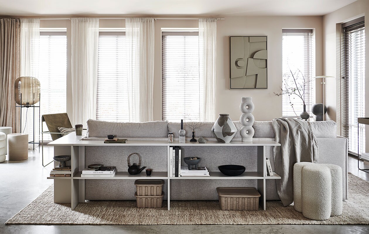 Verf op de muur Mushroom 142 (littlegreene). Ruime driezitsbank Cube in stof facet kiezel € 3610,- (studio-henk). Papierpulp dozen per 2 stuks vanaf € 35,- (misterdesign). Juten vloerkleed, 300×400 cm € 599,-, theepot met kopje € 35,99, gestreept kussen, 45×45 cm € 17,99, bordjes per stuk € 11,99, mok € 15,99, linnen plaid, 230×250 cm € 149,- (zarahome). Bouclé poef Clover van Pols Potten € 270,-, fauteuil Desert van Ferm Living € 249,30, metalen plantentafel van Ferm Living € 289,-, goudkleurige vloerlamp Reflection van Bolia € 509,99 (vtwonen.be). Vaas vlekken € 34,99, marmeren schaal op voet 29,99 (hm.com). Zwarte houten schaal van Urban Nature Culture € 52,95, mini-vaasje Vulca grey dots van Ferm Living € 15,- (nijhofbaarn). Overig privébezit.