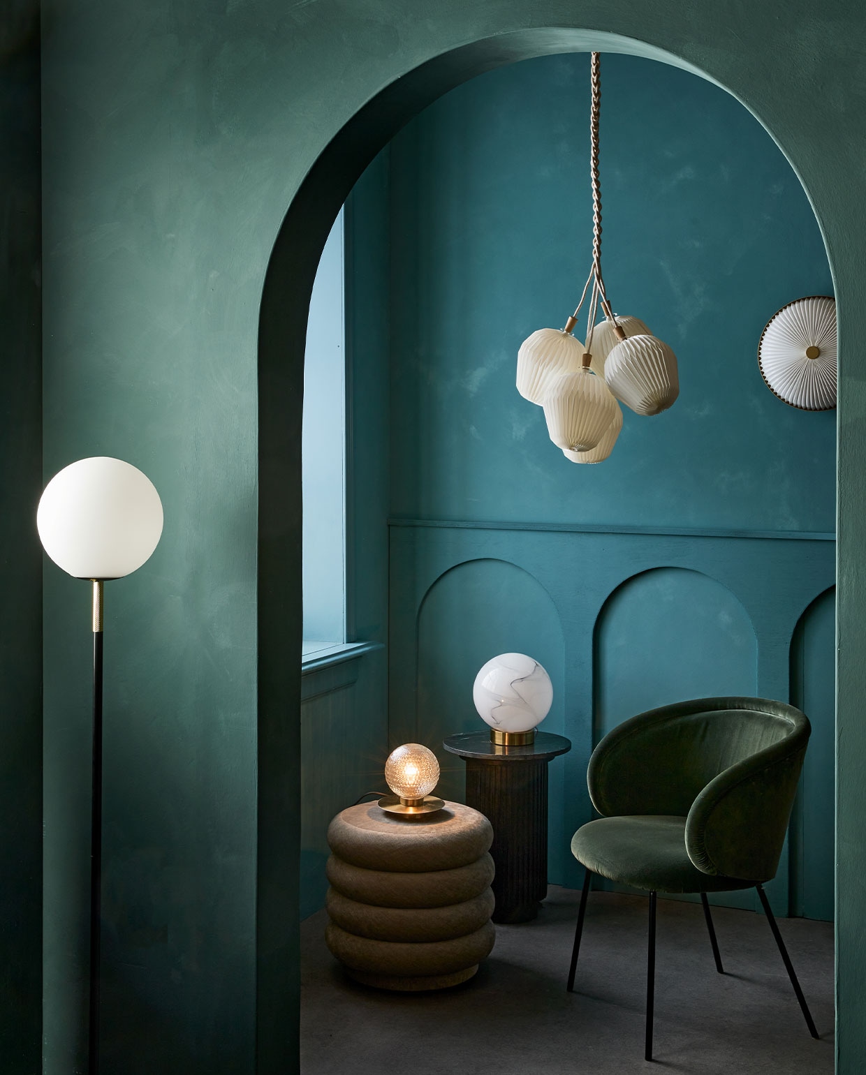 Kalkverf op de achterste muur 87 Petrol, op de muur met boog Staal/Steel 97, 2,5 liter € 126,- (lauthentique). Vloerlamp Orion van Zuiver € 195,-(vtwonen.be). Marmerlook tafellamp € 139,-, kleine gefacetteerde tafellamp met gouden voet € 98,-, zwarte marmeren bijzettafel € 419,89 (nordal.eu). Poef Faded Velvet van Ferm Living € 695,-, eetkamerstoel Ona vanaf € 968,- (edha-interieur). Wandlamp, 35 cm (Ø) € 628,-, hanglamp The Bouquet Chandelier Five Shades € 902,- (leklint.dk).