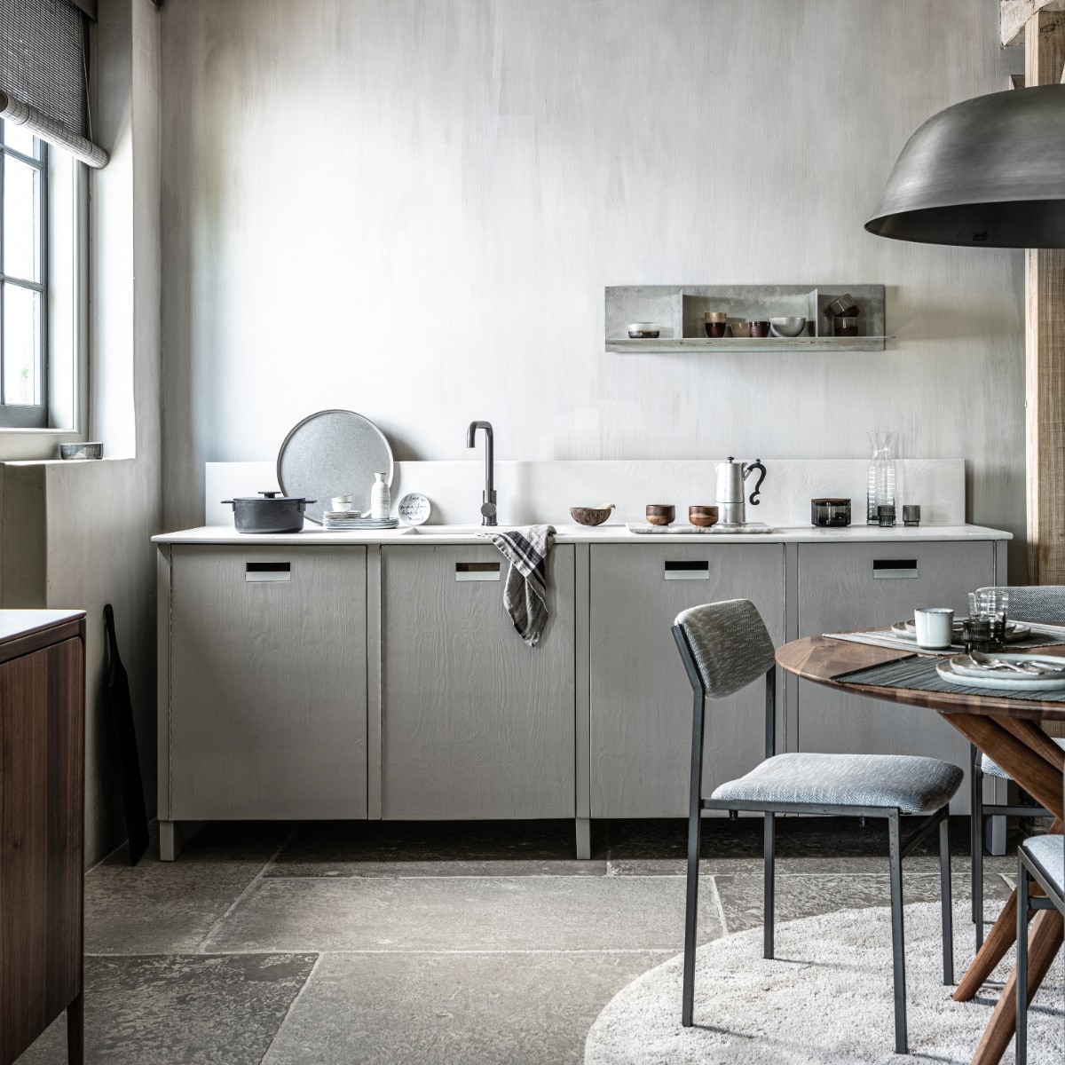 Op de wanden kalkverf Warm Grey van Pure &amp; Original 1 liter € 40,75 (pure-original.nl). Keuken op maat gemaakt, prijs op aanvraag (com-anders.nl). Kraan gun metal € 169,- (tworooms). Zwarte pan Surface van Serax € 126,-, glas Ripple van Ferm Living, set van 4 € 35,-, zwarte serveerplank Acacia van Bloomingville 70 cm € 60,99, houten theekop Collage van Serax, per stuk € 12,80 (vtwonen.be). Percolator Lady Anne € 59,-, tweekleurige keramieken mok Earth € 17,50, stonewashed rond stalen dienblad € 69,- (bymolle). Sake set € 39,75 (japansewinkeltje). Bordje met geschreven tekst van Anouk Kramer € 30,- (archive-store). Glazen opbergpot met houten deksel € 19,95, glazen karaf € 24,95 (nordal.eu). Wandplank Rivet, small, onbehandeld aluminium 87,6×24,4×20,6 cm (lxdxh) € 615,- (framacph.com). Hanglamp Cloche Three, geborsteld aluminium, 81×25 cm (Øxh) € 750,- (vanduivenboden). Vintage design stoelen met nieuwe stoffering € 850,-, walnoothouten eettafel Lakri 120 cm (Ø) € 2984,- (goeds). Gehamerd bestek, per stuk € 5,99, bamboe placemat, set van 2 € 6,99 (zarahome.com). Ronde borden van HK Living vanaf € 11,95, rechthoekige borden van Serax vanaf € 11,95, mok van HK Living € 6,95, schaal € 10,95 (loftloft). Walnoothouten dressoir Rikke € 2960,- (demachinekamer). Rond grijs vloerkleed € 3034,- (homestede). Roll-up gordijn bamboo flat sticks prijs op aanvraag (nature-deco.com).