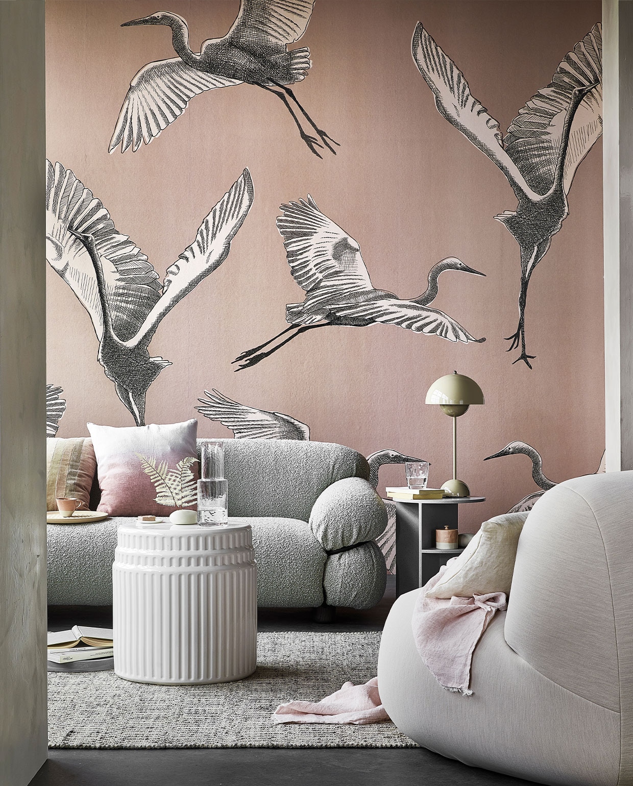 Digitaal behang Graphic Nature, 6 banen van 280×50 cm, totaal (lxb) 280×300 cm € 149,-. M.m.v. kasstoor.nl (bank, kussen met roze kleurverloop, salontafel van wit keramiek, bijzettafel van grijs keramiek, fauteuil), homestede.nl (grijze stenen schaal, houten dienblad, tafellamp), paviljoennoord.com (gestreept kussen, mini-bordje, amberblok), zara.com (kop, karaf, glas, roze pot met deksel), loods5.nl/design (vloerkleed), letoile.store (wit porseleinen vaasje, linnen kussen), bymolle.com (plaid), pure-original.nl (muurverf Fresco in kleur Ashes). Overig privébezit.