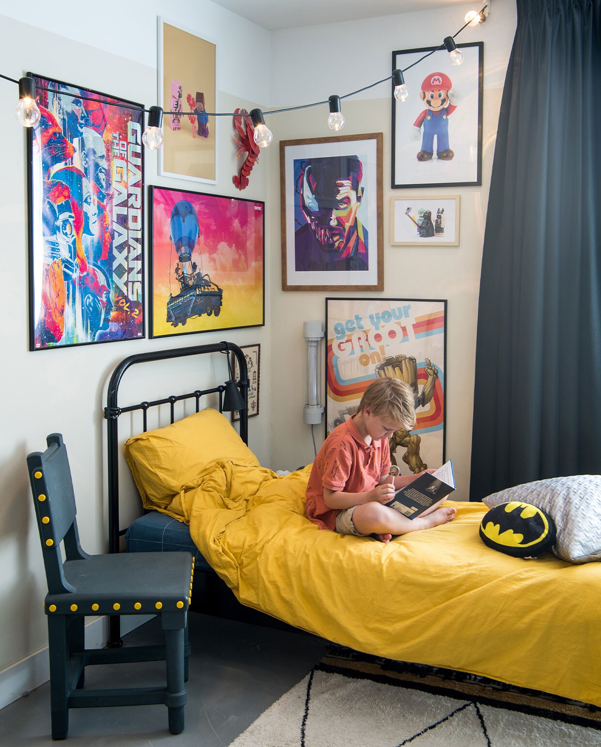 Stoel Studio Job, lichtsnoer Ikea, posterwand is combinatie van gekochte en zelf op maat gemaakte posters, kreeft Studio Roof, lamp aan bed Menu, lamp aan muur Fatboy, dekbedovertrekset H&amp;M, vloerkleed onbekend, Batman-kussen Kruidvat, zilveren kussen zelfgemaakt. Muurkleur RAL 1013, zwarte overgordijnen op maat gemaakt door stoffeerder.