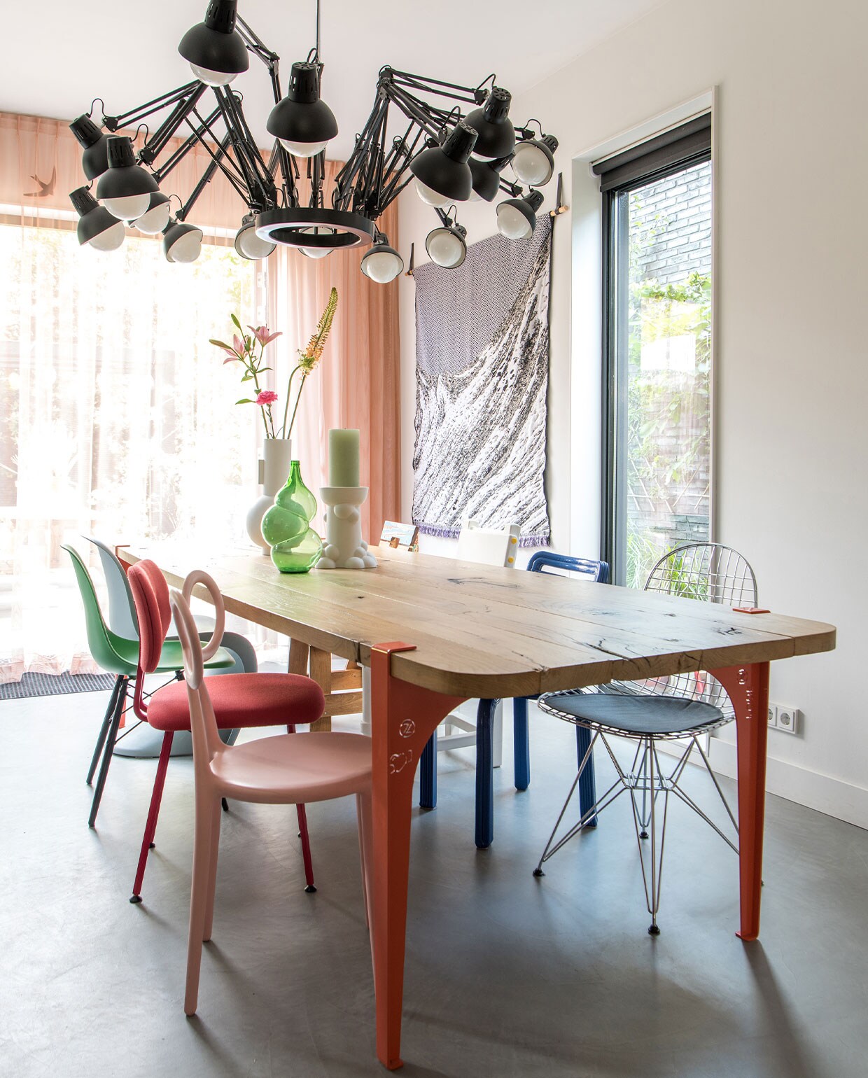 Lamp Dear Ingo van Moooi, eettafel eigen ontwerp by Maykel. Stoelen van linksvoor naar achter Qeeboo, Maarten Baas, Vitra, van rechtsachter naar voor Piet Hein Eek, Studio Job, Dirk Vander Kooij, Vitra. Witte vaas HKliving, bottle vaas Klaas Kuiken, witte kandelaar Jorine Oosterhoff via Cor Unum, wandkleed Plaid Skinn Throw No2 van Roos Soetekouw. Overgordijnen op maat gemaakt door stoffeerder, vitrage van Kvadrat-stof, kleur op muur onbekend.