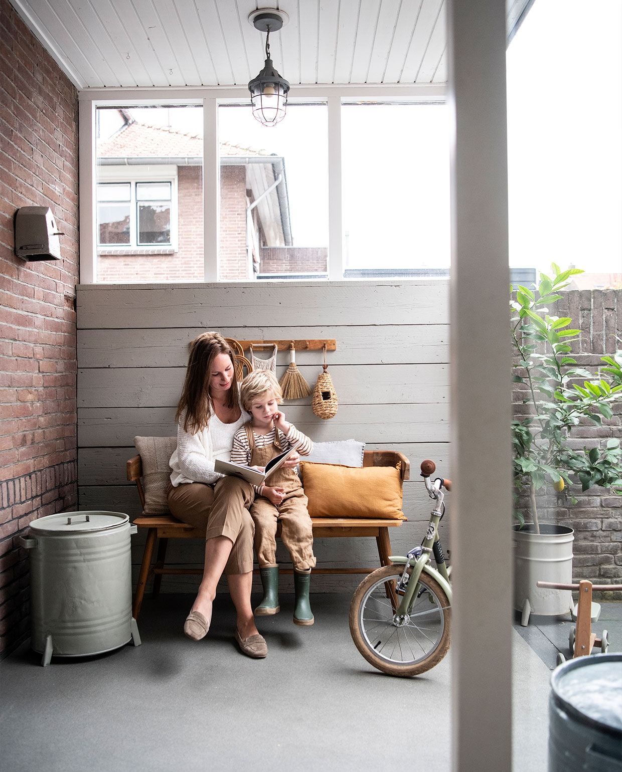 Bank Karwei. Bruin en grijs kussen Zara Home. Mosterdgeel kussen Sissy-Boy Homeland. Kapstok H&amp;M Home. Groen geverfde ronde bak Loods 5. Hanglamp V&amp;D. Kinderfiets Veloretti.