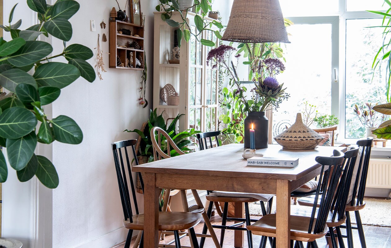 Vitrinekast via kennis, letterbak tweedehands. Planten Ficus benghalensis, Philodendron silver sword, potloodcactus, pannenkoekplant. Tafel en gevlochten mand tweedehands, Farstrup-spijlenstoelen Hit &amp; Run. Lamp zelfgemaakt van visnet, zwarte vaas D&amp;M Deco, kandelaar Rustik Lys.