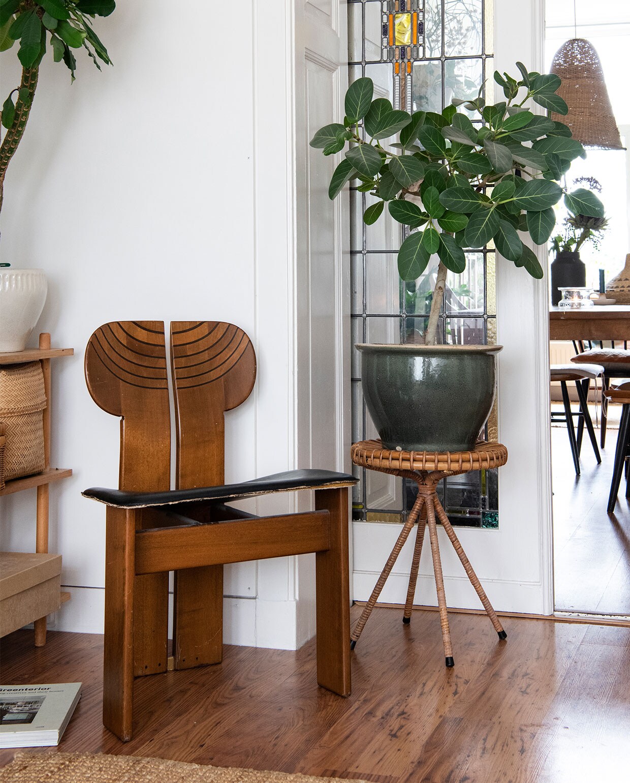 Stoel vintage, rotan tafel en grote pot tweedehands, kleed Ikea, planten Euphorbia Madagascar Jewel, Ficus benghalensis. Tafel en gevlochten mand tweedehands, Farstrup-spijlenstoelen Hit &amp; Run. Lamp zelfgemaakt van visnet, zwarte vaas D&amp;M Deco, kandelaar Rustik Lys.