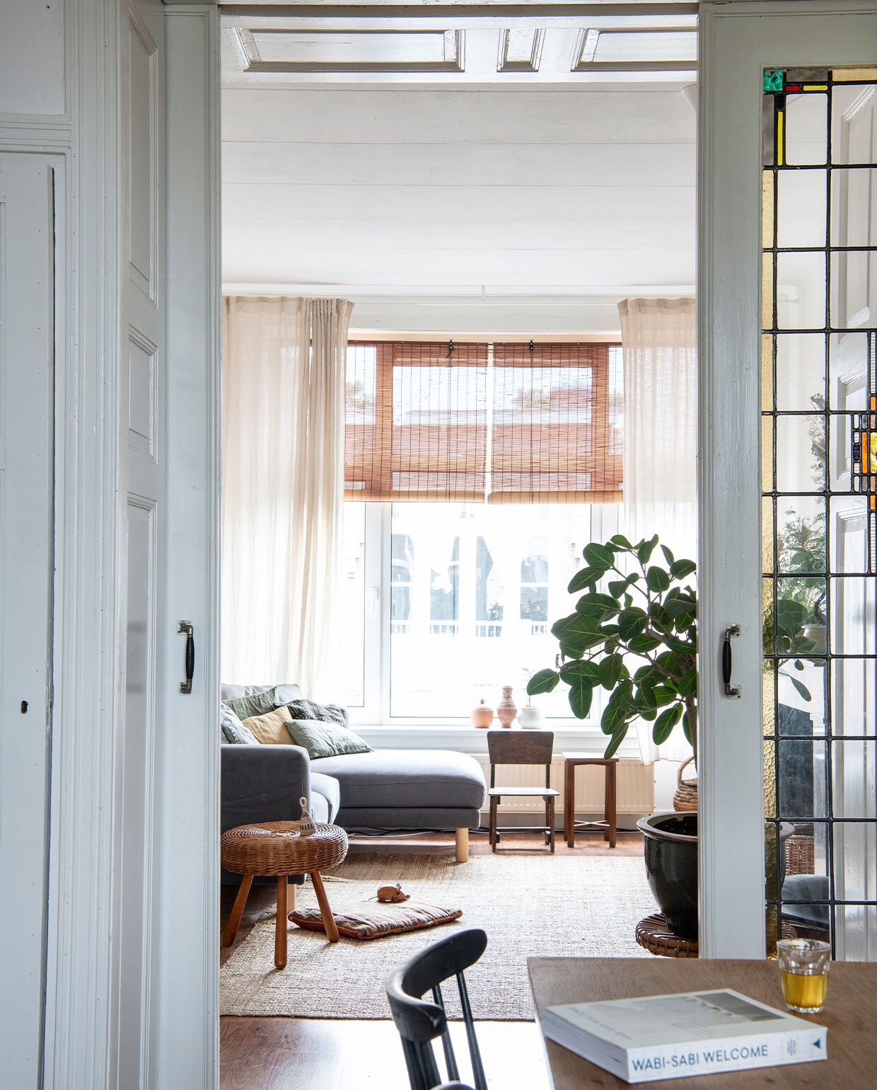 Stoelen en krukken tweedehands. Bank en kleed Ikea, gordijnen H&amp;M Home, rolgordijnen bol.com. Grote plantenpot tweedehands, plant Ficus benghalensis. Overig herkomst onbekend.