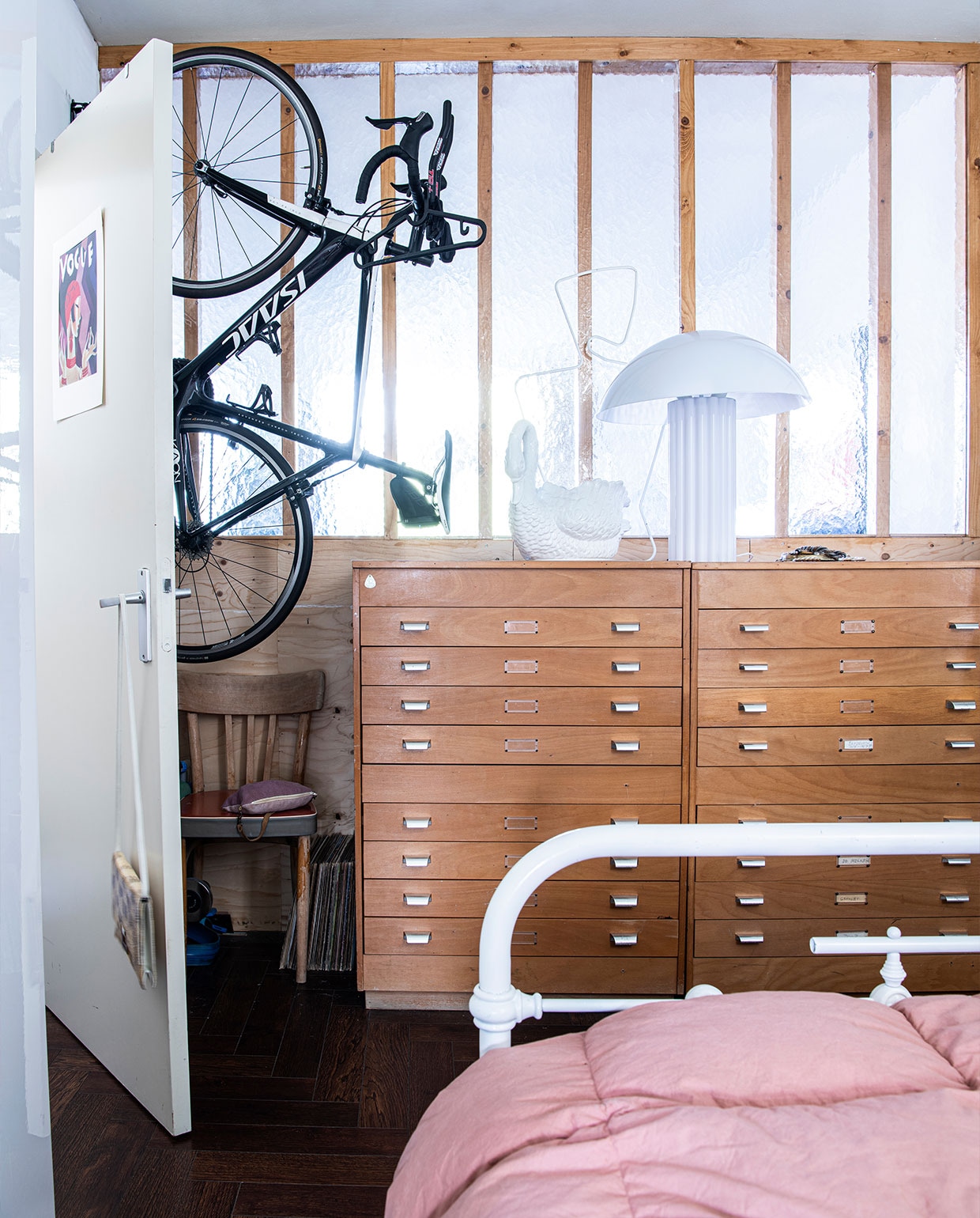 Poster op de deur souvenir uit Parijs. Handtas aan de deur dorisvintage.nl. Stoel Noppes. Archiefkast Gideon Italiaander. Witte zwaan en bed erfstuk. Witte lamp HKliving. Bedlinnen Kwantum. Fiets Isaac Cycle.