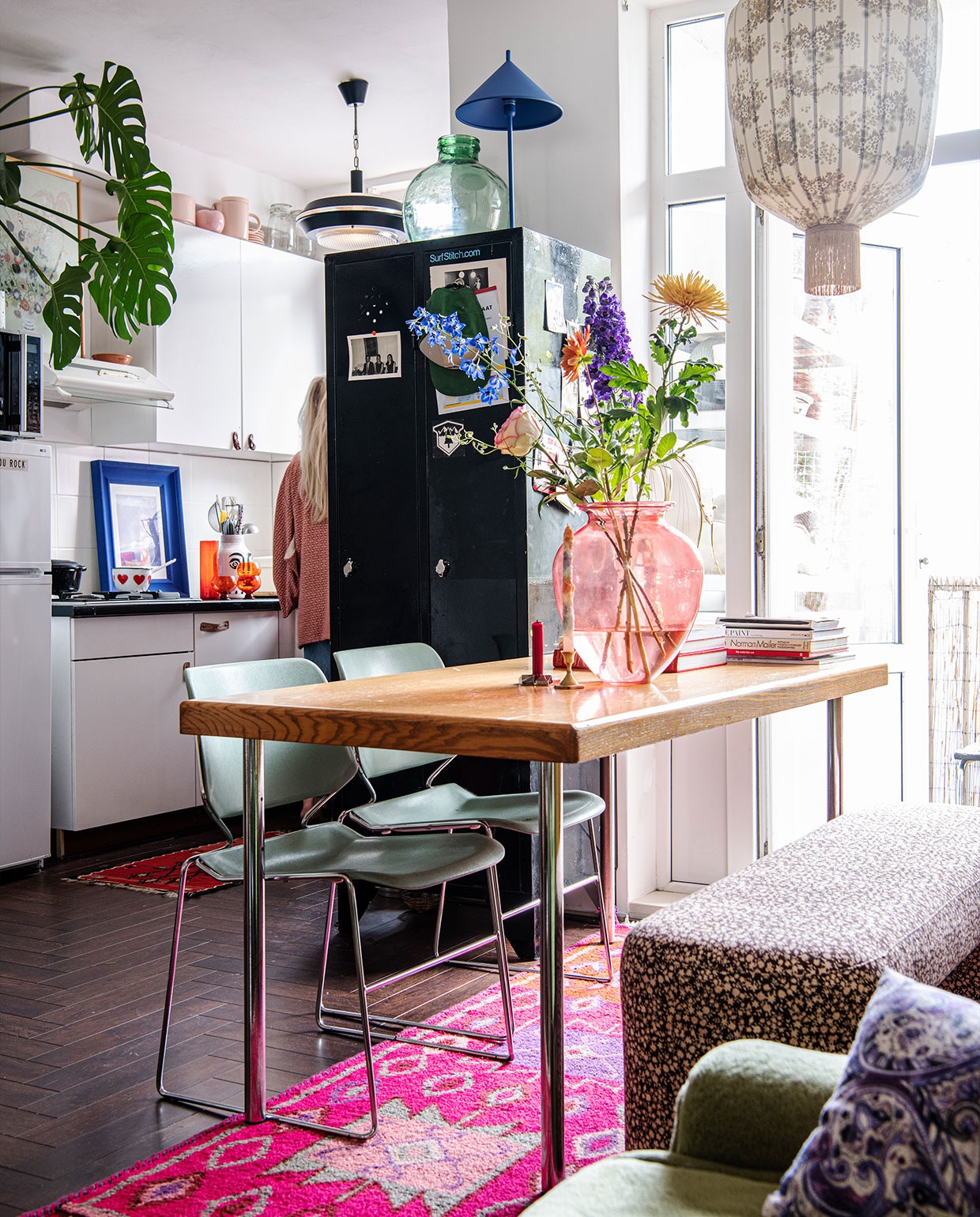 Kussens, roze tapijt en bankje Doris voor HKliving. Blauwe lamp op kast, oranje glaswerk en rood vloerkleed keuken HKliving. Hanglampen Vintage Depot. Leren handvatten keukenkasten zelfgemaakt van leren riem. Pot Pols Potten. Blauwe lijst Ikea. Steelpan erfstuk. Roze servies op de keukenkasten Nørd conceptstore.