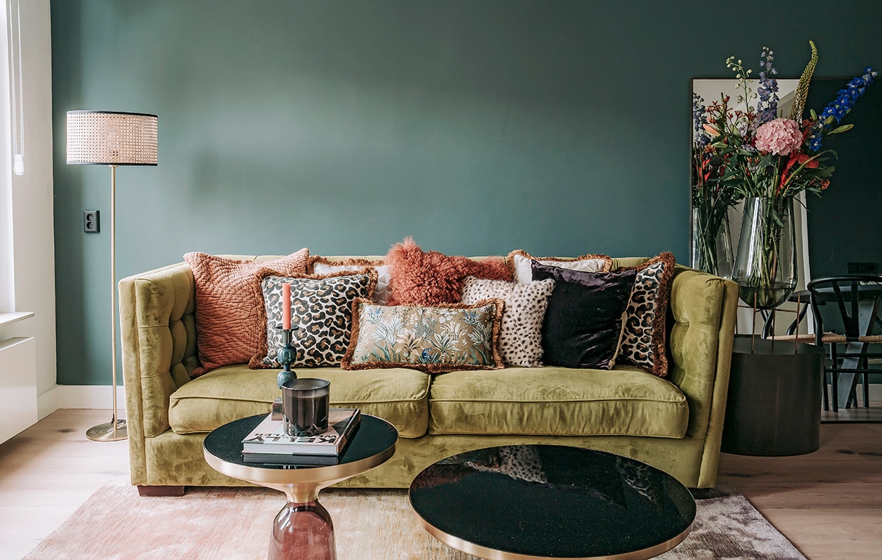 Vouwgordijnen Jan Sikkes, muurverf Inchyra Blue van Farrow &amp; Ball. Bank Rofra Home. Kussens, vloerkleed, poef en kandelaar Nox Studio Interiors. Bijzettafels Classicon, geurkaars, staande lamp Zara Home.Koffietafelboek Kelly Wearstler.