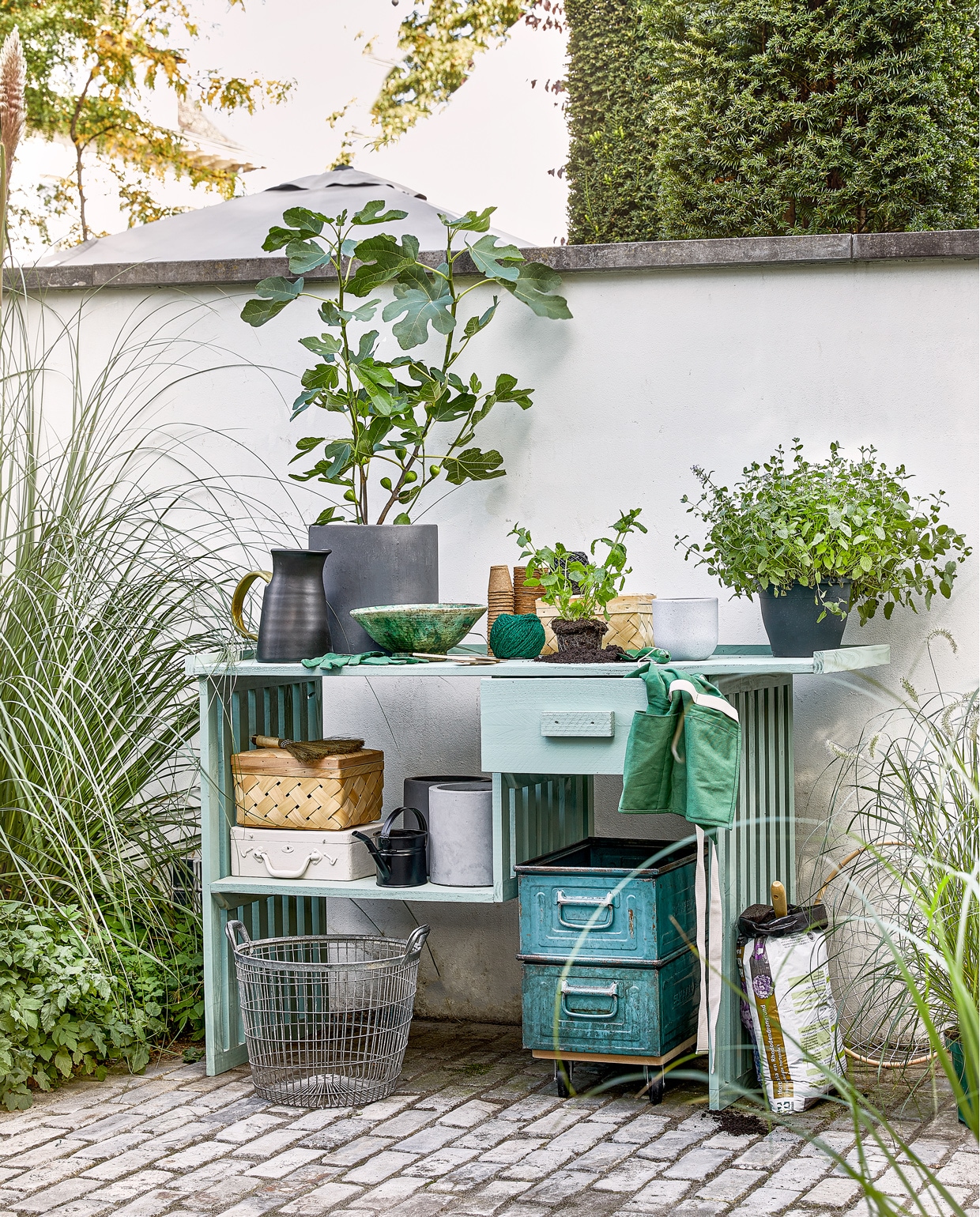 Hoge antracietkleurige cementpot Cilindro € 24,99, klos groen kokostouw € 4,99, klos zwart bindbuis € 4,49, biologisch afbreekbare kweekpotjes € 2,89 per 18 stuks, grijze cilinder plantenpot € 4,99, zak potgrond € 1,99, draadschaal € 24,50 (intratuin.be). Keramieken gieter € 40,99 (vtwonen.be). Tuinhandschoenen € 4,95, handschepje € 4,95, handveger € 15,95, zwarte gieter € 7,95, tuinschort € 14,95 (dille-kamille.be). Schaal € 22,50 (householdhardware.com). Palmblad mandjes € 5,78 per set (sostrenegrene.com). Witte kist € 12,50 (vandijkenko.nl). Meubeltransporter € 9,99 (gamma.nl).