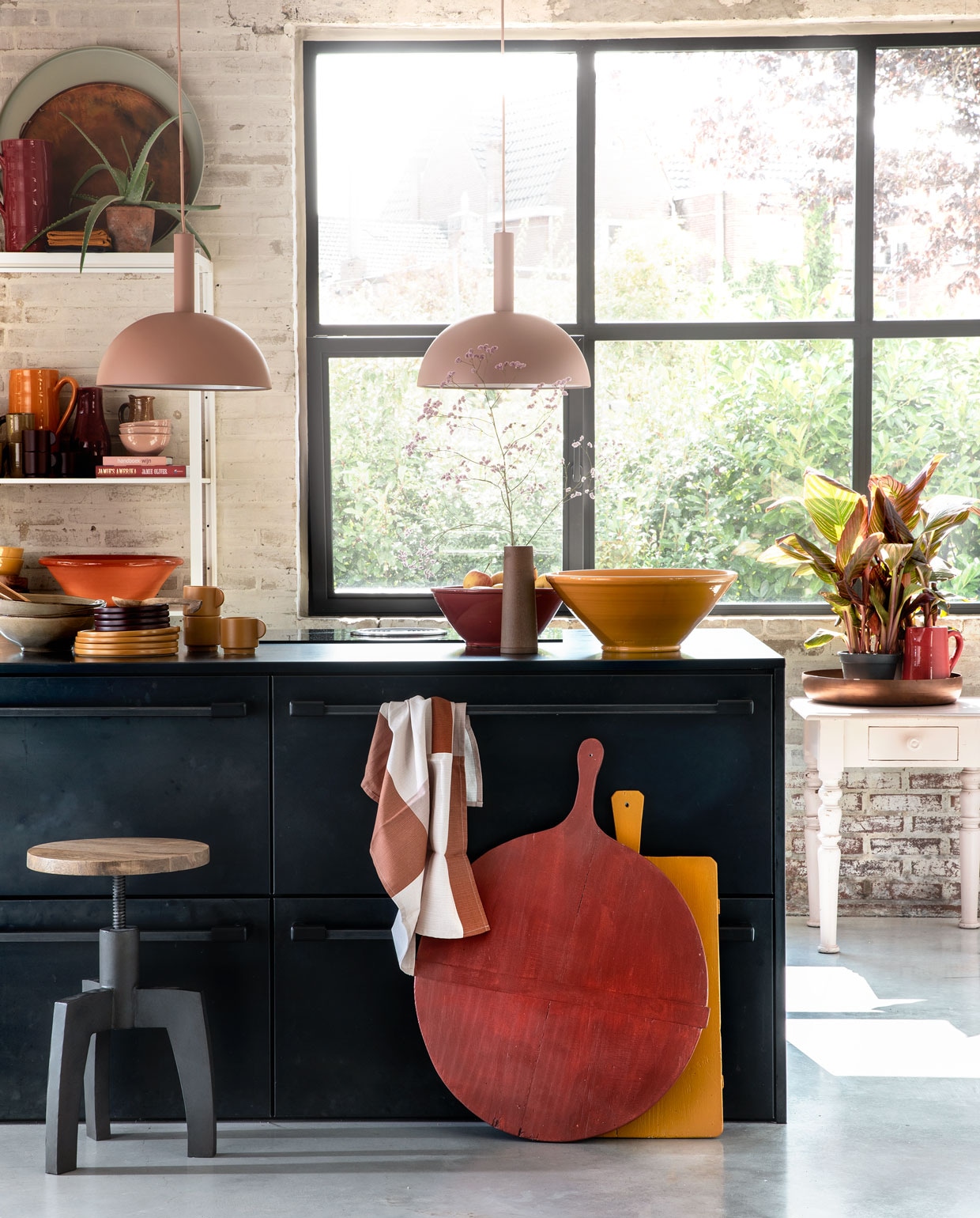 Zachtroze hanglampen Dome Shade van Ferm Living inclusief roze fitting high per stuk € 269,- (vtwonen.nl). Draaikruk Space van BepureHome € 99,- (Woondock). Grote oude kaasplanken per stuk € 35,- (H&amp;M Home), gelakt met Perfection zijdeglans lak in dieprood en mosterdgeel, 750 ml € 25,99 (Histor). Theedoek € 4,99, okergele kopjes per stuk € 5,99, okergele borden per stuk € 7,99, donkerpaarse borden per stuk € 4,99 (H&amp;M Home). Okergele schaal € 35,-, donkerrode schaal € 25,- (In-Petto). Beige schalen per stuk € 12,49 (Intratuin). Bovenop de kast: grote donkerrode kan € 35,- (In-Petto), theedoeken in okergeel en donkerpaars per stuk € 4,99 (H&amp;M Home), koper­kleurige schaal van BePureHome € 39,95, zachtgroene schaal € 24,95 (Woondock). Midden in de kast: zachtroze schaaltjes per stuk € 7,50, okergele kan € 35,- (In-Petto). Donkerpaarse kopjes per stuk € 5,99 (H&amp;M Home). Donkerrode karaf Nikki € 21,99, lichtbruine karaf € 8,99 (Intratuin). Beige kan € 8,99 (Intratuin). Onder in de kast: terracotta schaal € 35,-, okergele diepe borden € 12,50 (In-petto). Zachtroze tafeltje € 175,- (Combitex). Koperkleurige schaal Big Waitress van BePureHome € 24,95 (Woondock). Donkerrode kleine kan € 25,- (In-Petto). Kamerplanten Canna Hybride per stuk € 9,99 (Intratuin). De keuken is een eigen ontwerp van de bewoners, binnenwerk van hout, blad en kasten afgewerkt met blauw staal. Overig privébezit.