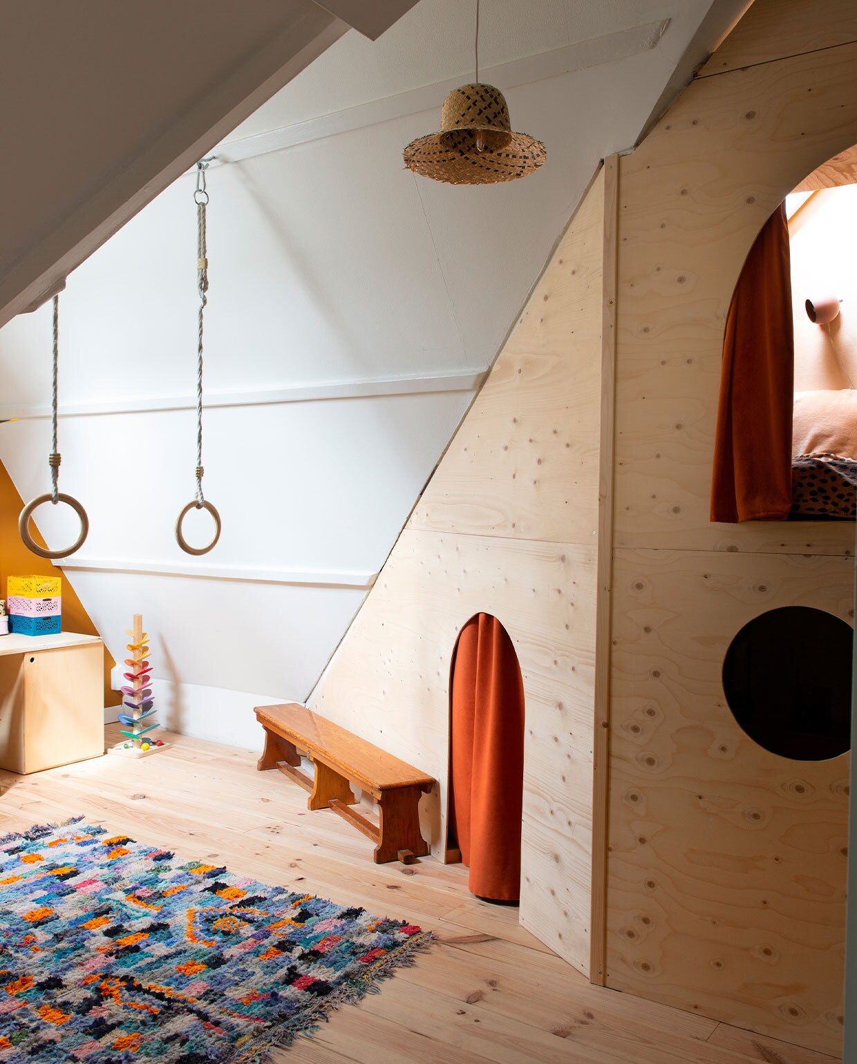 Boucherouite vloerkleed El Ramla Hamra. Ringen De Bruine Schommel. Rieten hanglamp zelfgemaakt van een strohoed van Ikea. Vintage gymbank. Bed en bureau zelfgemaakt. Vloer blank gelakt vurenhout.