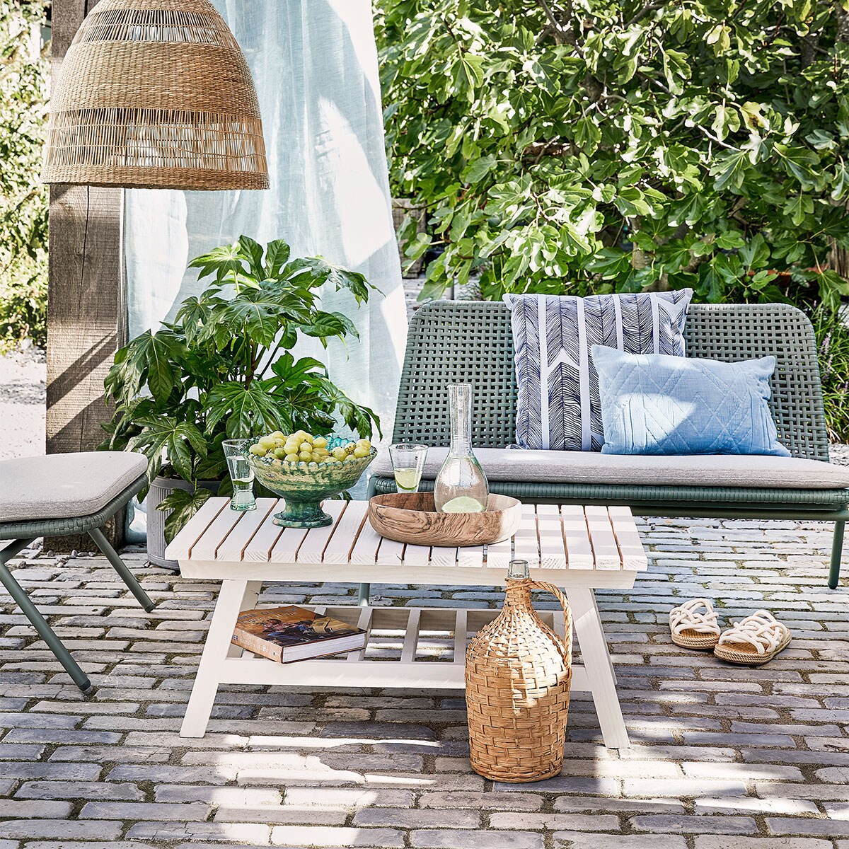 Bank Wivinia € 419,- en stoel Wivinia € 211,50 van Kave Home (vtwonen.be). Gordijn gemaakt van linnen stof per meter € 25,- (ochreandred). Kussen met print Heringbone € 25,95, lichtblauw kussen Naida € 19,99 (intratuin.be). Schaal op voet € 99,95, walnoothouten schaal € 75,-, glazen karaf Cigogne € 23,50, glazen op voet Diabolo per stuk € 6,80 (householdhardware.nl). Instappers € 35,99 (zarahome.com). Rieten lamp Torared € 39,95 (ikea.com). Plaid Native Fan € 34,99 (sissy-boy.com). Sisal kussen € 25,- (loods5.nl). Overig privébezit.