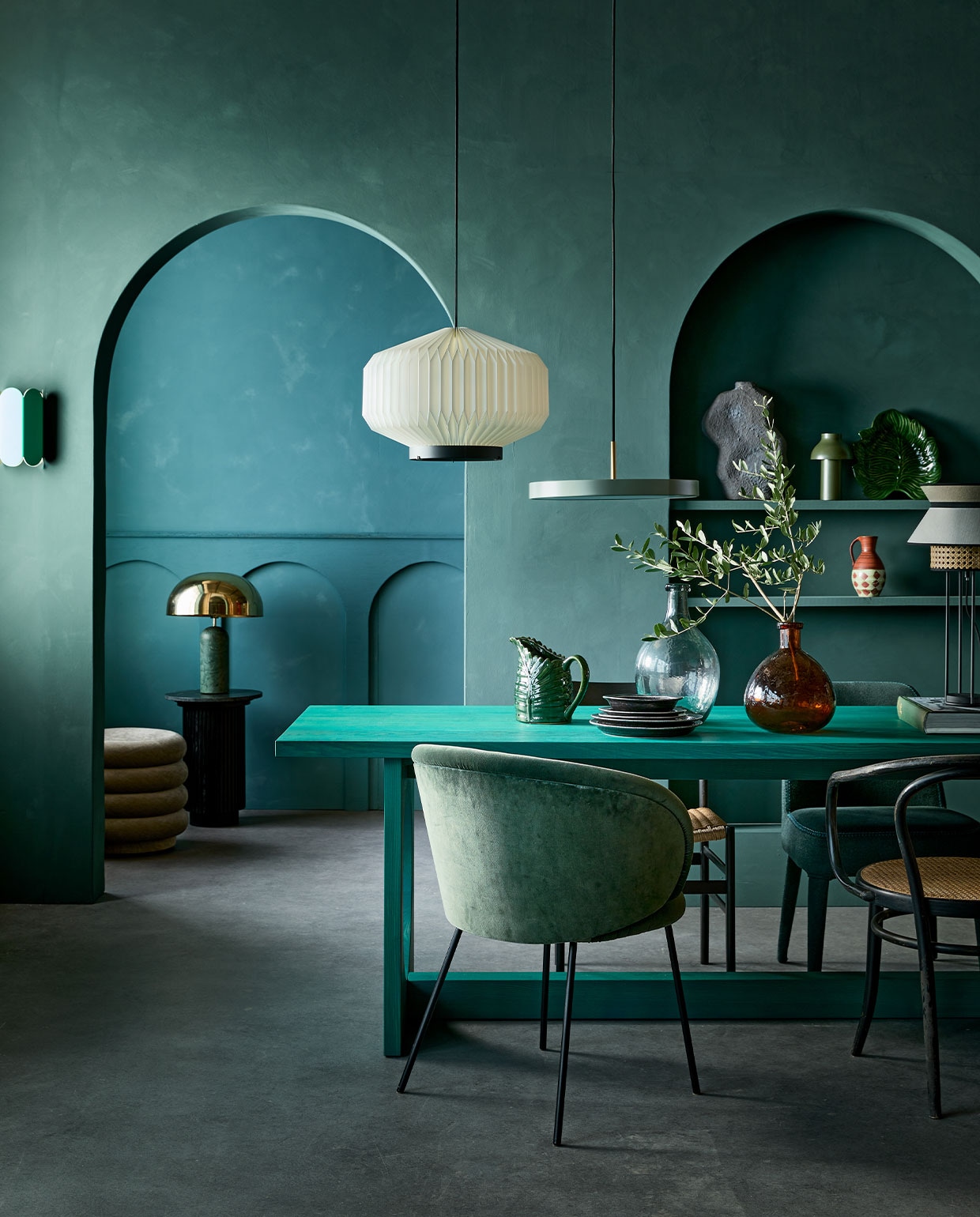 Kalkverf op de achterste muur 87 Petrol, op de muur met bogen Staal/Steel 97, 2,5 liter € 126,- (lauthentique.nl). Witte geplisseerde hanglamp Lamella Gold, 35 cm (Ø) € 838,- (leklint.dk). Groene metalen hanglamp Asteria van Umage € 289,-, groene tafellamp PC Portable van Hay op plank € 89,10, groene wandlamp Arcs van Hay € 215,- (vtwonen.be). Poef Faded Velvet van Ferm Living € 695,-, eetkamerstoel Ona vanaf € 968,-, eetkamerstoel Febo vanaf € 1177,- (edha-interieur.nl). Tafellamp met marmeren voet en gouden kap € 435,-, marmeren bijzettafel € 419,89 (nordal.eu). Groene kan met bladvorm € 35,-, schaal met bladpatroon € 37,50 (maisonnl.com). Vintage vaasje in kast € 15,- (vandijkenko.nl). Grijze sculpturale vaas links op plank vanaf € 79,- (lanena-home.com). Zwarte eetkamerstoel met cord zitting, per 4 € 1000,- (vintagehoarder.com). Zwarte dinerborden, per stuk € 21,90, kleine zwarte borden, per stuk € 18,90, groene flesvaas € 37,25, bruine flesvaas € 33,95 (iblaursen.nl). Tafellamp Singapour van Market Set met webbing en kap € 293,- (fonq.nl). Eettafel Loop van Sarah Trenité for design label Bowden Cable, exclusief verkrijgbaar bij Friday Next Studio, prijs op aanvraag (fridaynext.nl). Overig privébezit.