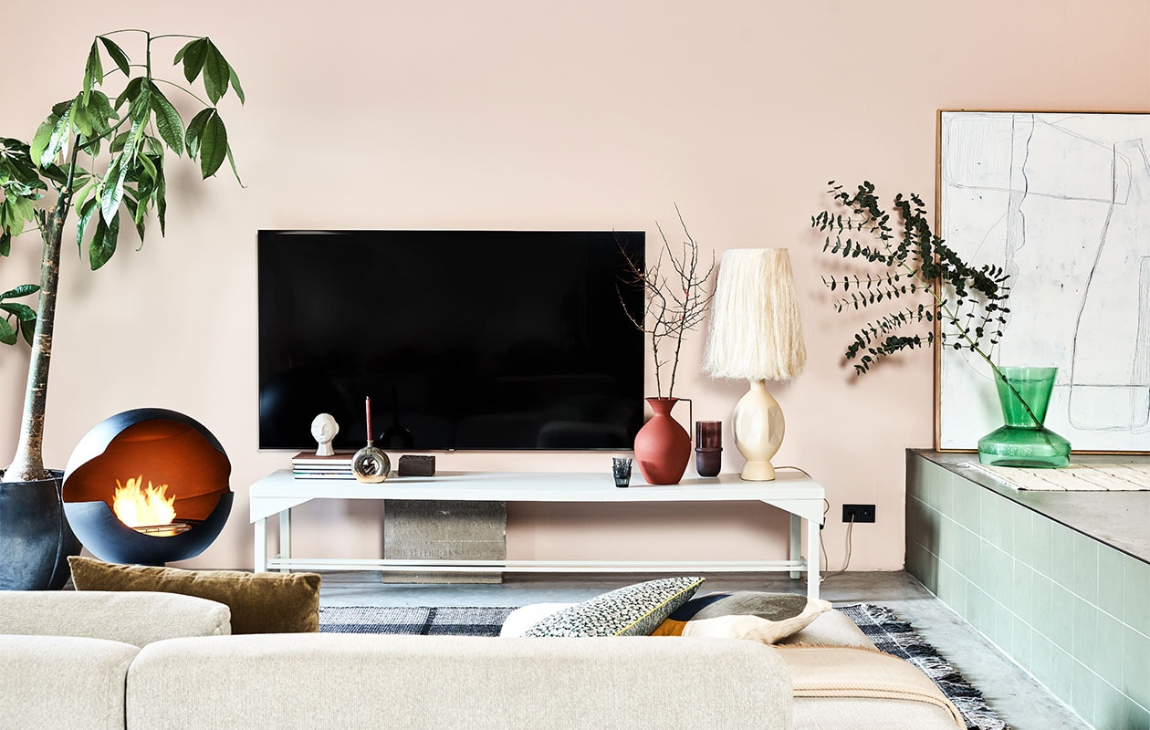Televisie Samsung 82TU8000, 82 inch € 1349,- (samsung). Sidetable, 59x248x50 cm (dxbxh), prijs op aanvraag (combitex). Bio-ethanol haard Vauni, 60x58x90 cm (bxdxh) € 3195,- (haardcenter). Zandkleurige aardewerken lampenvoet Boho, 58 cm (h) € 189,-, handgemaakte lampenkap Boho Abaca, 28×56 cm (Øxh) € 179,-, donkergroen velvet kussen, 60×40 cm (bxh) € 29,95, kussen met bloemenprint van by Doris voor HKliving, 35×60 cm (bxh) € 37,95, wit kunstwerk Brutalism, 123×163 cm (bxh) € 595,-, groene glazen bijzettafel Hk-mta2860 gebruikt als vaas € 229,- (hkliving). Ronde vaas van Bloomingville, hier gebruikt als kandelaar, 19,5 cm (h) € 36,95, ecomix gerecycled papier-maché hoofd van vtwonen, 20 cm (h) € 34,95, houten blokkandelaar van vtwonen, 15x15x7,5 cm (bxdxh) € 19,95, donkerrode vaas van Pols potten, onderdeel van set van 3 € 220,-, bruine glazen vaas Belise, 11×18,5 cm (Øxh) € 39,90, crèmekleurig kussen van Bloomingville, 40×40 cm € 49,90 (vtwonen.be). Karpet Jazz, 160×230 cm € 415,- (zuiver). Plaid op de bank, 140×190 cm € 35,99 (zarahome.com). Ecru wollen vloerkleed, 80×130 cm (ottomania.nl). Overig privébezit.