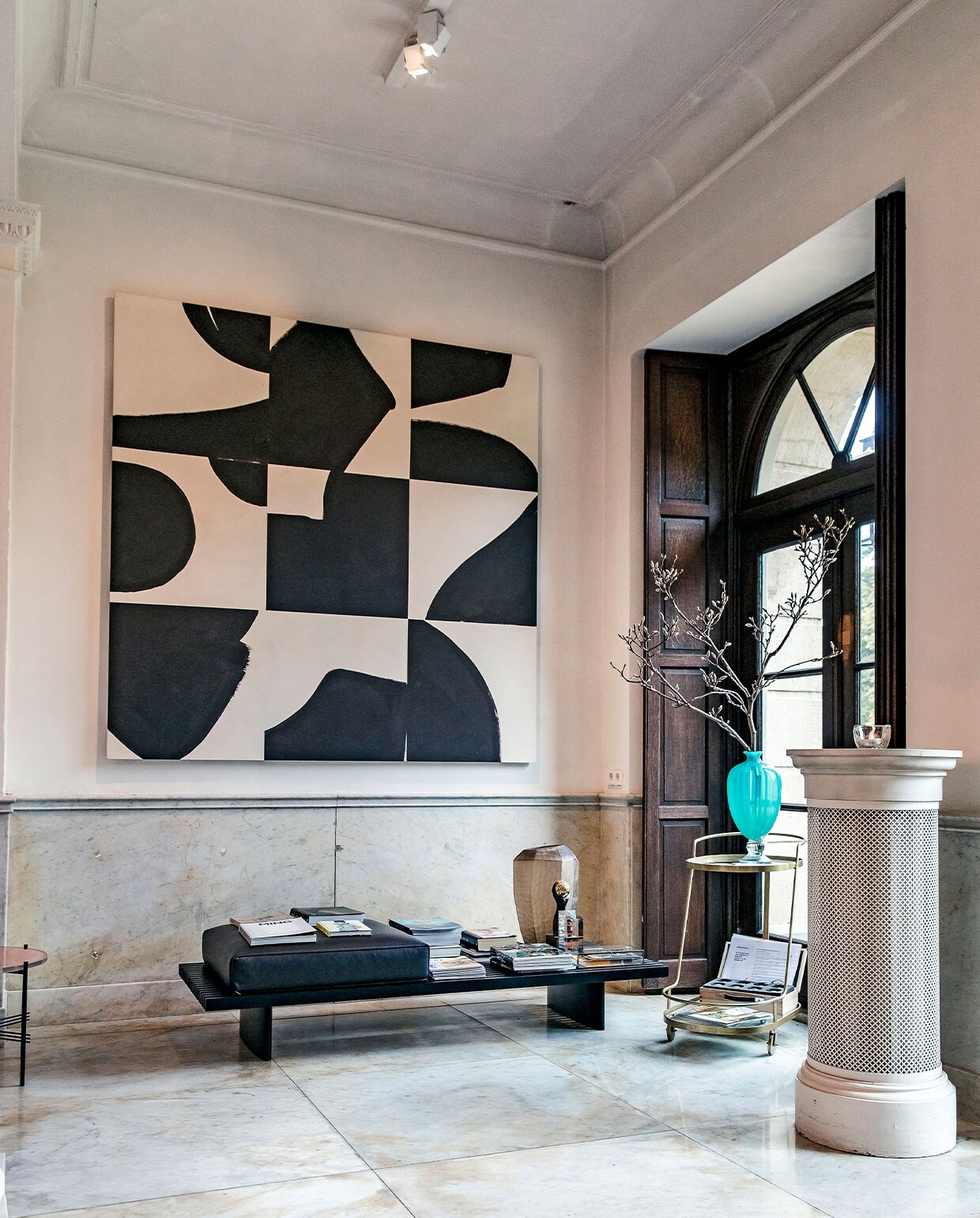 De entreeruimte van het hoofdhuis zet meteen de toon: klassieke elementen – zoals een marmeren vloer, lambrisering en donkere, houten luiken – in combinatie met moderne toevoegingen, zoals een strakke bank en XL abstract kunstwerk.
