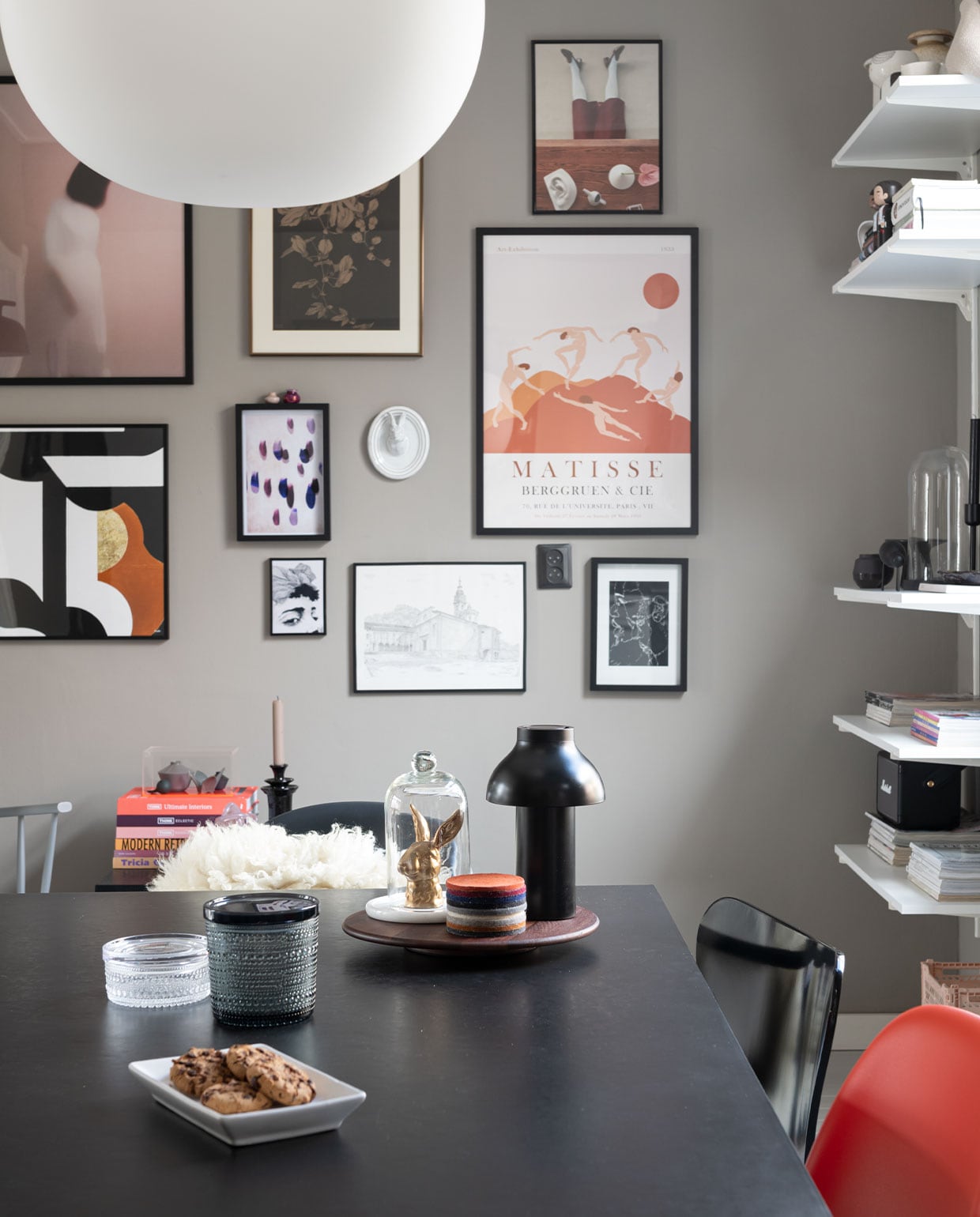 Stoel J110, wandlamp Hay, kussen zelfgemaakt. Hanglamp Glo Ball S2 van Flos. Vloerkleed en vitrinekist HKliving, minivaasjes Hella Duijs. Zwarte bijzetter Westwing, kandelaar Day. Konijn Vintage Fever, onderzetters Nio &amp; Elva. Potten Iittala. Wandlamp Ambit van Muuto. Kunst v.l.n.r.: print vrouw Mia Wallace via Ruben Ireland, H&amp;M. Haas papier-maché Babettes Wereld, tegel Studio Job van Koninklijke Tichelaar, posters vrouw en print druppel en gezicht Juniqe. Minivaasjes op lijst van bevriende kunstenaar. Print roze vrouw Gurille Design, grafische print Part 2 Terra van Atelier Andrea. Passiebloem van Anton Pieck uit ouderlijk huis. Keramieken hazenkop Des Pots. Print Matisse Pstr studio. Tekening Zwitserse kerk door plaatselijke kunstenaar. Print Rechtszaak van Studio Abeelen. Muurverf Authentic Grey van Flexa. Eettafel en zwarte lamp Hay,. Konijn Vintage Fever. Panton Chairs van Vitra, vacht sheepy.cc.