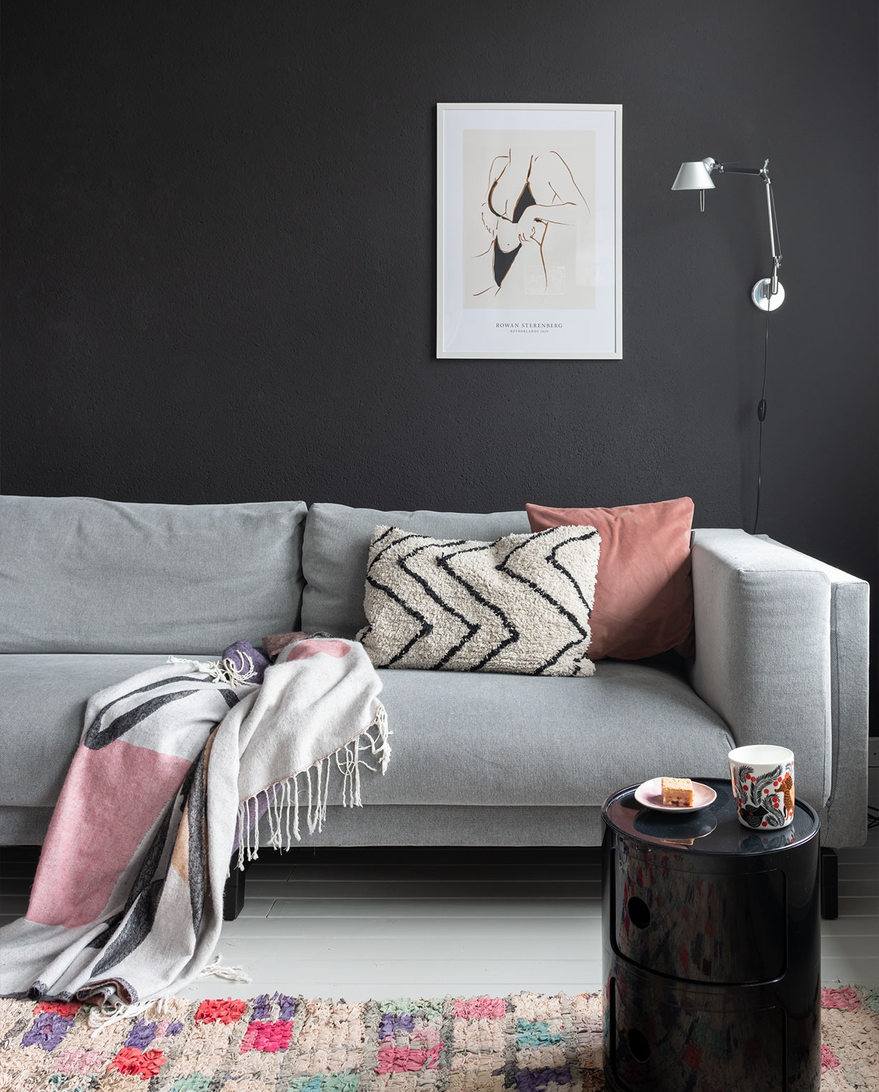 Bank Ikea, zwart kastje Componibili van Kartell. Hanglamp en beige kussen HKliving, wandlamp Tolomeo van Artemide. Vintage Boucherouite kleed van Trendcarpet, roze kussen Particolare, plaid Sissy-Boy Homeland. Glaswerk Iittala, zwarte kandelaar Normann Copenhagen, spiegel Kwantum. Muurkleur Raaf van Histor. Schuifdeuren via vhdeuren.nl. Houten vloer gelakt met NyLo topcoat kleur 7044.