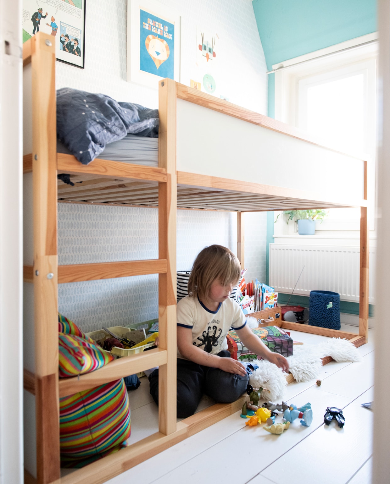Bed Ikea. Gestreept Alexander Girard-kussen Vitra. Behang Studio Ditte. Muurverf, vloerverf Soft Pearl van Flexa. Mand Ferm Living. Print met naam Samuel Etsy. Franse Kuifje-poster en leren koffer familiebezit. Krat Hema, mand Sissy-Boy. Beddengoed Ikea, vacht Noordermarkt Amsterdam. Overig onbekend.