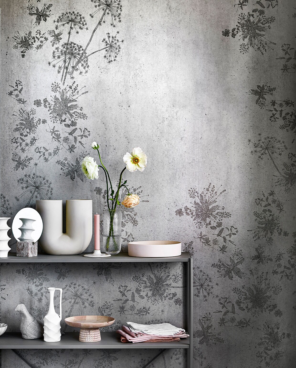 Digitaal behang Wild Flower Concrete, 6 banen van 280×50 cm, totaal (lxb) 280×300 cm. M.m.v. loods5.nl (stellingkast), loods5.nl/design (witte vazen uit set van vier, roze schaal), hm.com (spiegel in marmeren blok), kasstoor.nl (U-vormige vaas, houten etagère), letoile.store (kandelaar, roze theedoeken), bolia.com (glazen vaas, gebroken-witte schaal), homestede.nl (stoffen vogel), paviljoennoord.com (schalen met geschulpte rand, witte theedoeken), hm.com (glazen gieter). Overig privébezit.