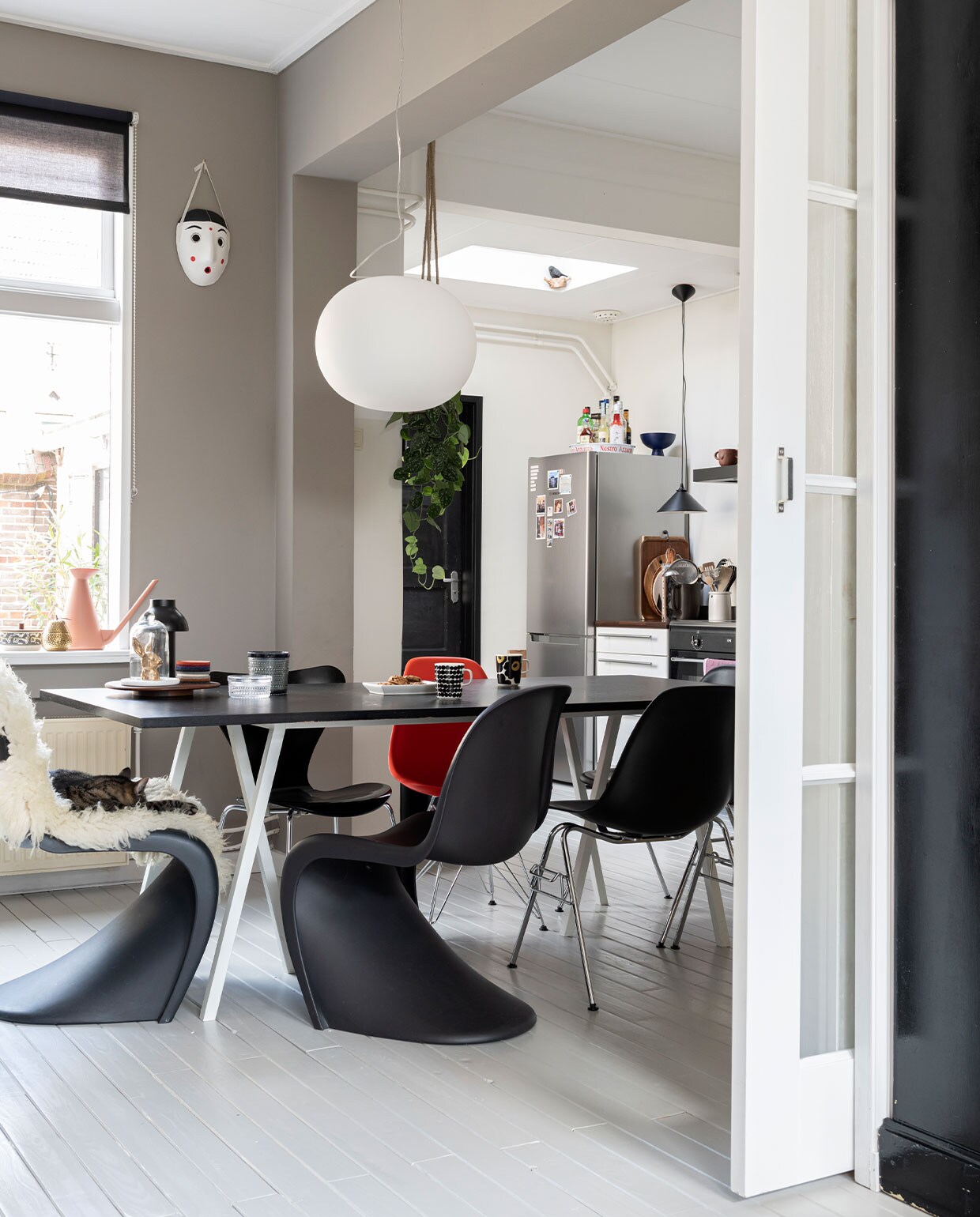 Eettafel Loop Stand en zwarte lamp van Hay, stoelen Panton Chairs, Eames-stoel DSR en Eames-stoel DSS van Vitra. Vlinderstoel Fritz Hansen. Hanglamp Glo Ball S2 van Flos. Hanglamp keuken vintage. Vacht sheepy.cc. Konijn Vintage Fever.. Glaswerk Iittala. Onderzetters en Marimekko-mokken Nio &amp; Elva. Masker en gieter Hay. Messing peer H&amp;M. Dienbladen en snijplanken Habitat en Ikea. Dienblad op koelkast souvenir uit Italië. Blauwe schaal Raawii. Potten House Doctor. Keukenapparatuur Bosch en Smeg. Muurverf Authentic Grey van Flexa.