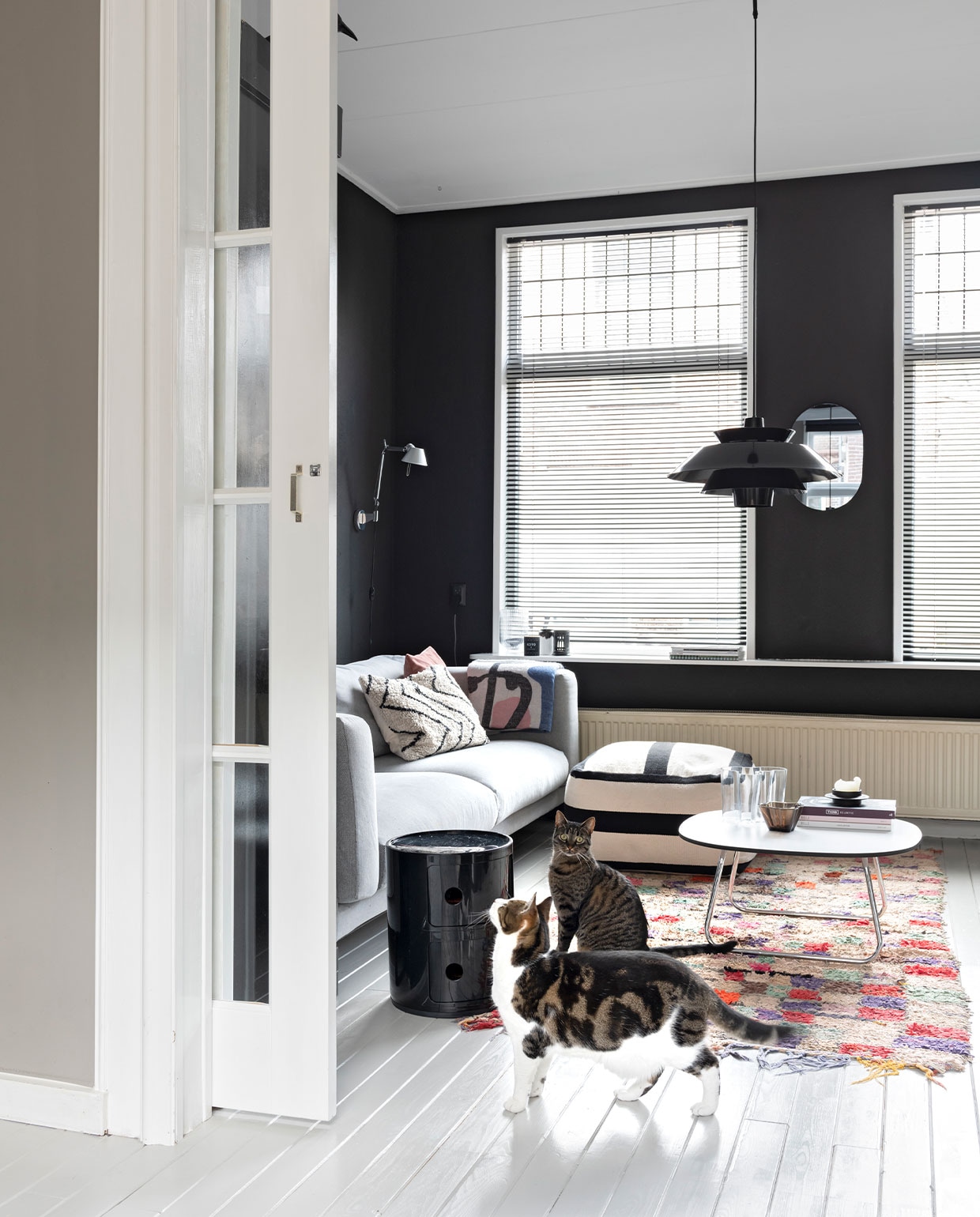 Bank Ikea, poef van Aai Made with Love, salon­tafel van Artifort via Marktplaats, zwart kastje Componibili van Kartell. Hanglamp en beige kussen HKliving, wandlamp Tolomeo van Artemide. Vintage Boucherouite kleed van Trendcarpet, roze kussen Particolare, plaid Sissy-Boy Homeland. Glaswerk Iittala, zwarte kandelaar Normann Copenhagen, spiegel Kwantum. Muurkleur Raaf van Histor. Schuifdeuren via vhdeuren.nl. Houten vloer gelakt met NyLo topcoat kleur 7044.