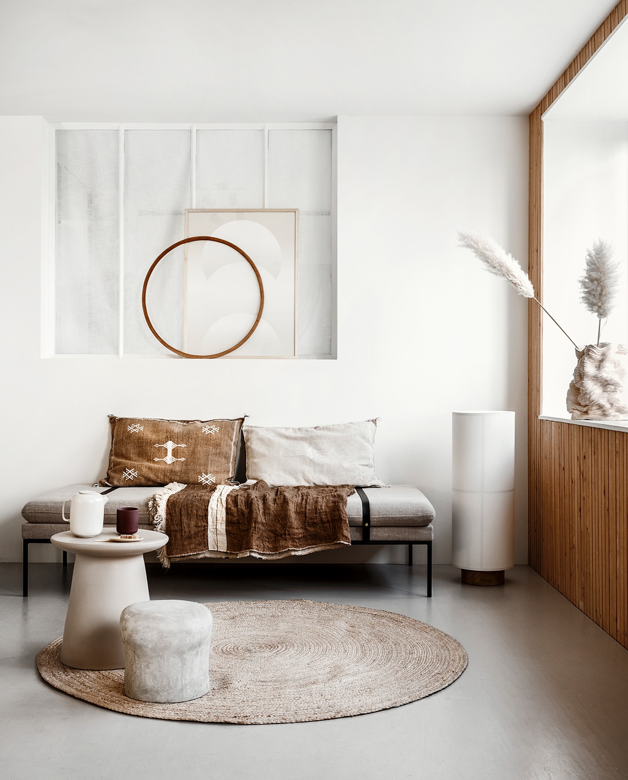 Daybed van Ferm Living met leren banden(kolkenkolk). Rieten mat van Nordal, Ø 150 cm (vtwonen.be). Vloerlamp Hashira (menudesignshop.com). Bijzettafel van keramiek (boer-staphorst). Betonnen kruk van FCK (serax.com). Kussens met fijne borduursels (zenzaliving.com). Linnen doek Bruges stripe (libeco.com). Grafische print, handgemaakte vaas (2222studio.com). Houten cirkel privébezit.