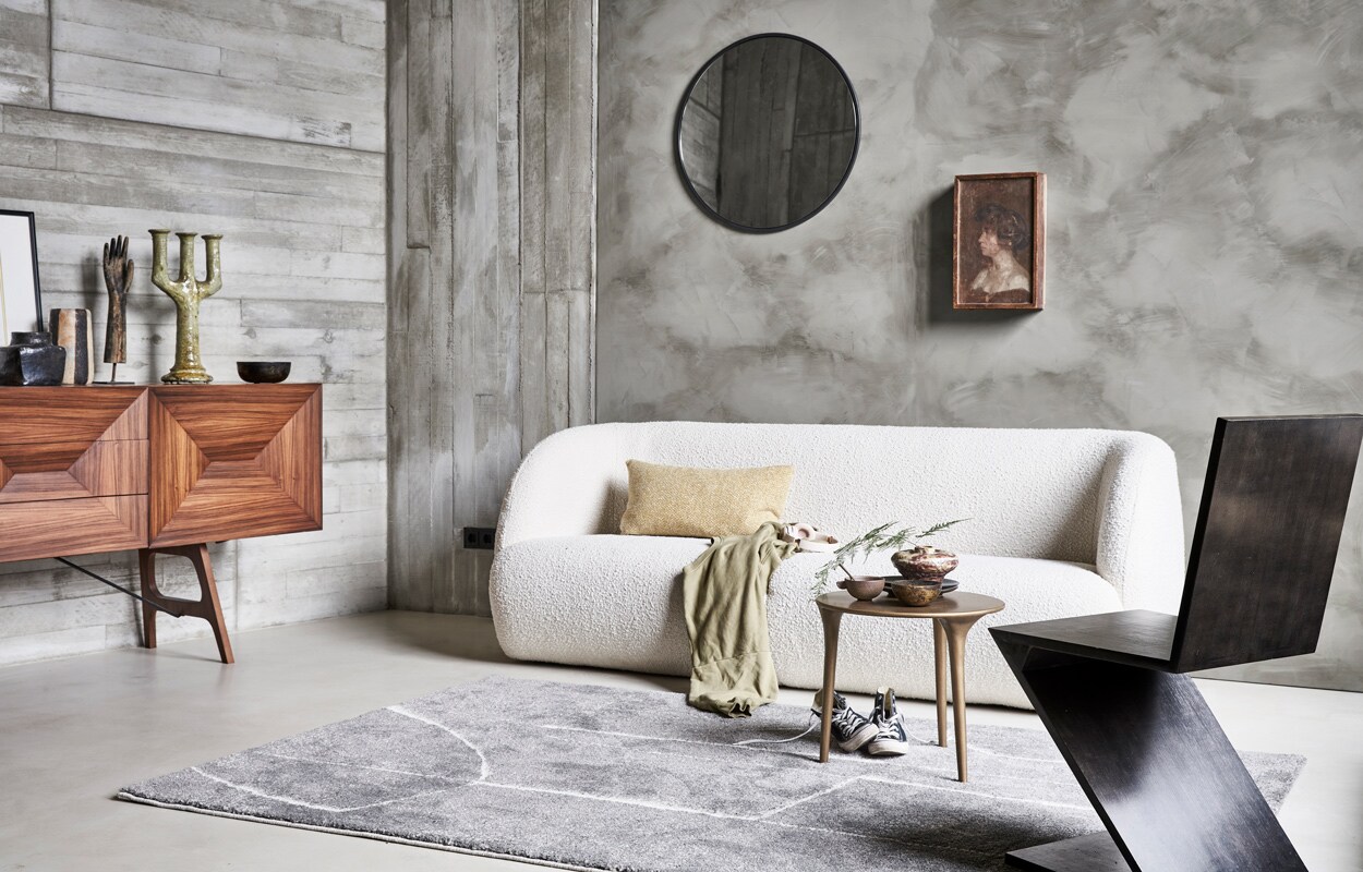 Vloerkleed Abstract in grijs,160×230 cm € 199,-.M.m.v. pure-original (muurverf Fresco in de kleur Tundra), sofacompany.com (bank), couleurlocale.eu (salontafel, kussen, vazen, schaal, spiegel), vintage­hoarder.com (dressoir, hand op voet, stoel), converse.com (gympen), vtwonen.nl (plaid van Marc O’Polo). Overig privébezit.