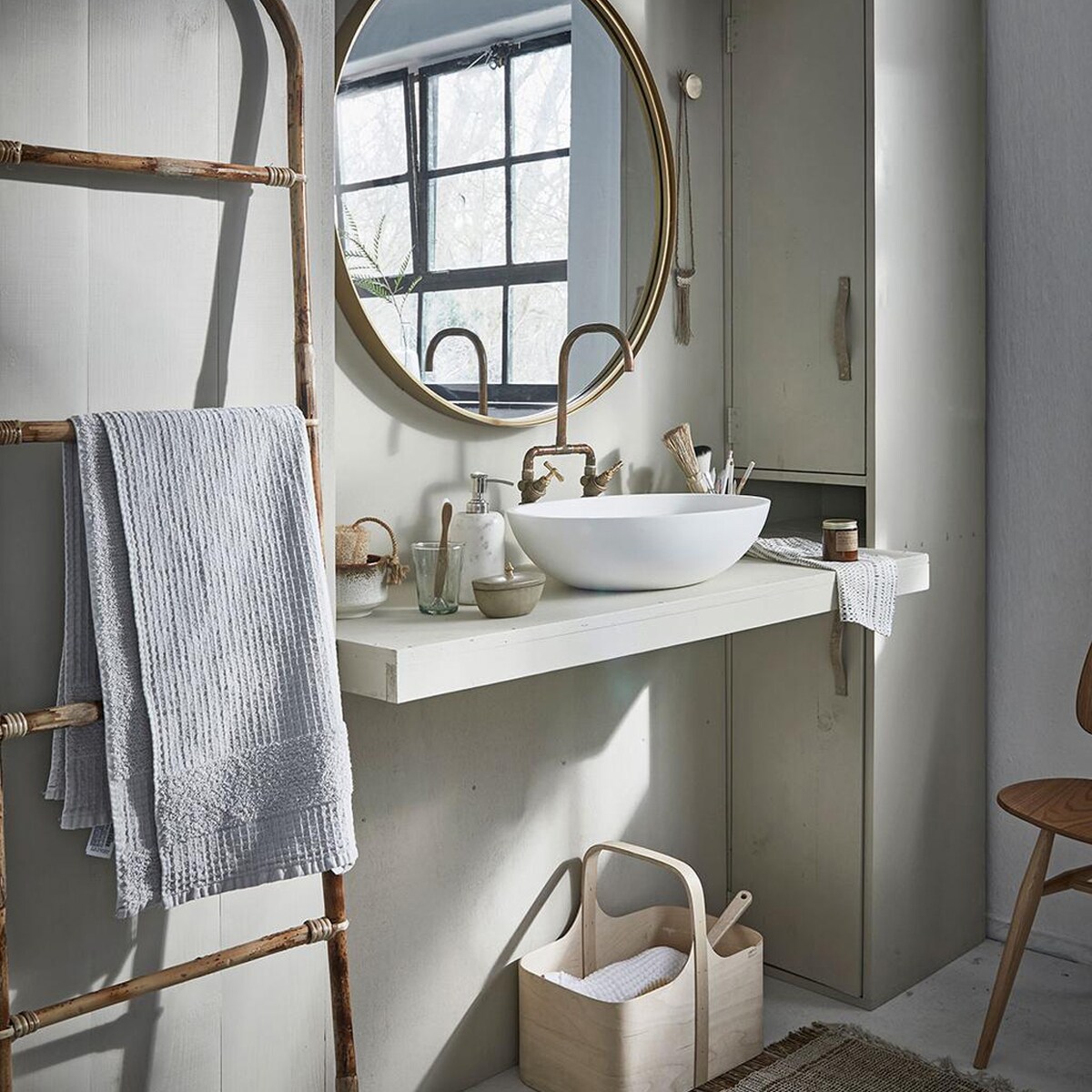 Grote ronde spiegel, marmeren zeeppomp (Nordal). Bamboe ladder, vloerkleed (Madam Stoltz). Witte wafeldoek (De Weldaad). Stoel Butterfly van Ercol (De Machinekamer). Berkenplex opbergmand (Nordic New). Grijze handdoek (Zara Home). Waskom Girona (Ton Scholten). Kraan (Jan van IJken Oude Bouwmaterialen). Tadelakt zandkleurig potje met deksel (MaisonNL). Bureaulamp (Vint. Amersfoort). Glas, linnen doek in opbergzak, witte opgerolde wafeldoek (De Weldaad). Zandkleurig met bruine kom, messing muurknop van Ferm Living, geurkaars in bruin glazen potje (Six and Sons). Rieten mand in kast vanaf (H&amp;M Home). Badborstel (Dille &amp; Kamille). De kast is geschilderd in de kleur Bone van Farrow &amp; Ball (De Ru). De muur is geschilderd in de kleuren Egg White en Light Grey van vtwonen (Karwei).