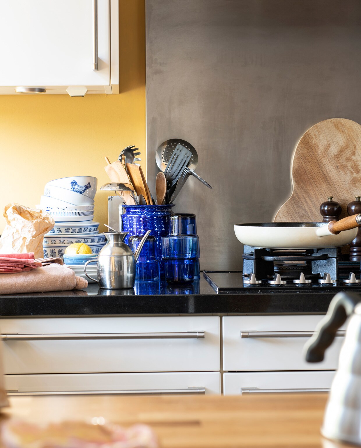 Keuken Siematic, muurverf India Yellow van Farrow &amp; Ball via De Ru. Glazen en plank Iittala. Kommen van een Chinese toko. Pot Arket. Schaaltjes &amp;klevering, kleinste schaaltje zelf geboetseerd. Pan Le Creuset.