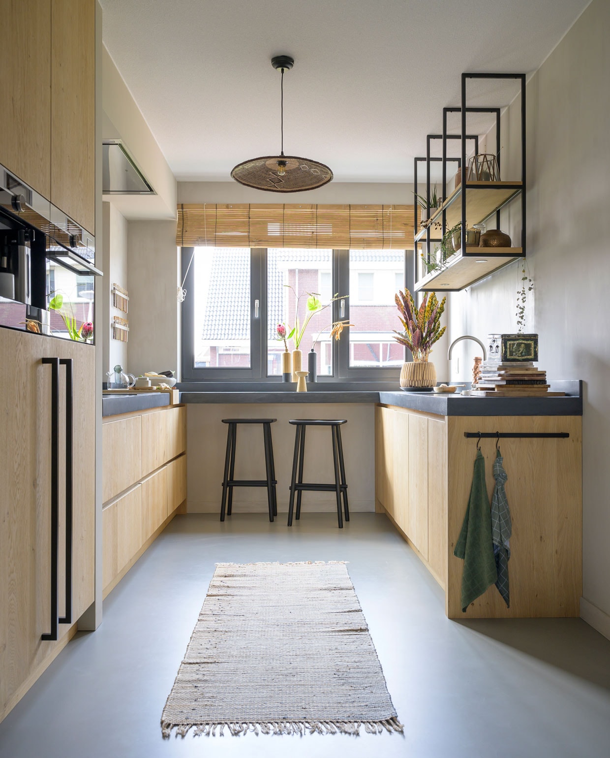 Zelfontworpen keuken Van Lieshout keukens &amp; interieur. Apparatuur AEG. Beton ciré werkblad Beal. Hanglamp Casa Gitane. Krukken Butt van vtwonen. Rolgordijn Bamboo Import Europe. Vazen op de bar erfstuk oma. Vloerkleed Madam Stoltz. Herkomst plantenpot onbekend. Theedoekenrek onderdeel van de keuken.