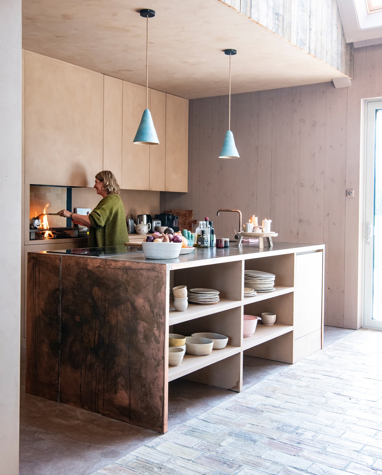 Keuken en kookeiland ontworpen door Larissa. Werkblad en kraan Hotbath. Kookplaat Inventum. Lampenkappen keramist Loeke Pam. Servies eigen ontwerp, in samenwerking met Loeke Pam. Achter grill chamotte haard­tegels Van Scheppingen. Op de vloer oude Franse tegels via Jan van IJken Oude Bouwmaterialen. Tableau voor kaarsen Ikea. Op de kasten kalkverf Topaze van Pure &amp; Original, op de wand Rose Dust van Pure &amp; Original, via Piccolina Schilderwerken. Overig herkomst onbekend.