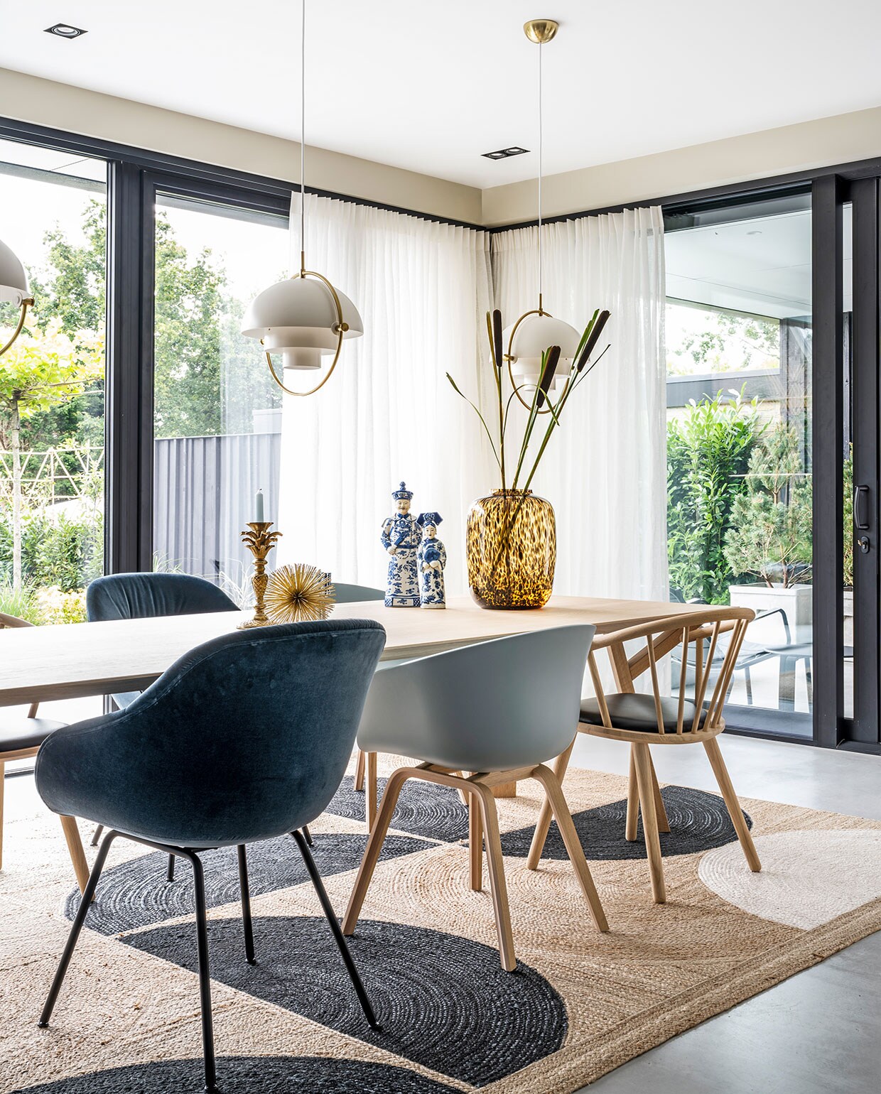 Hanglampen Multi-Lite Gubi, tafel Arp Design, vloerkleed Élitis, donker- en lichtblauwe stoelen Hay, houten stoelen zwarte zitting Bolia, gouden stekelitem Loods 5, kandelaar palmboom Anna+Nina, beelden Asian Mix Interior, vaas Artic Cheetah Vase the World, linnen gordijnen van Interstil.