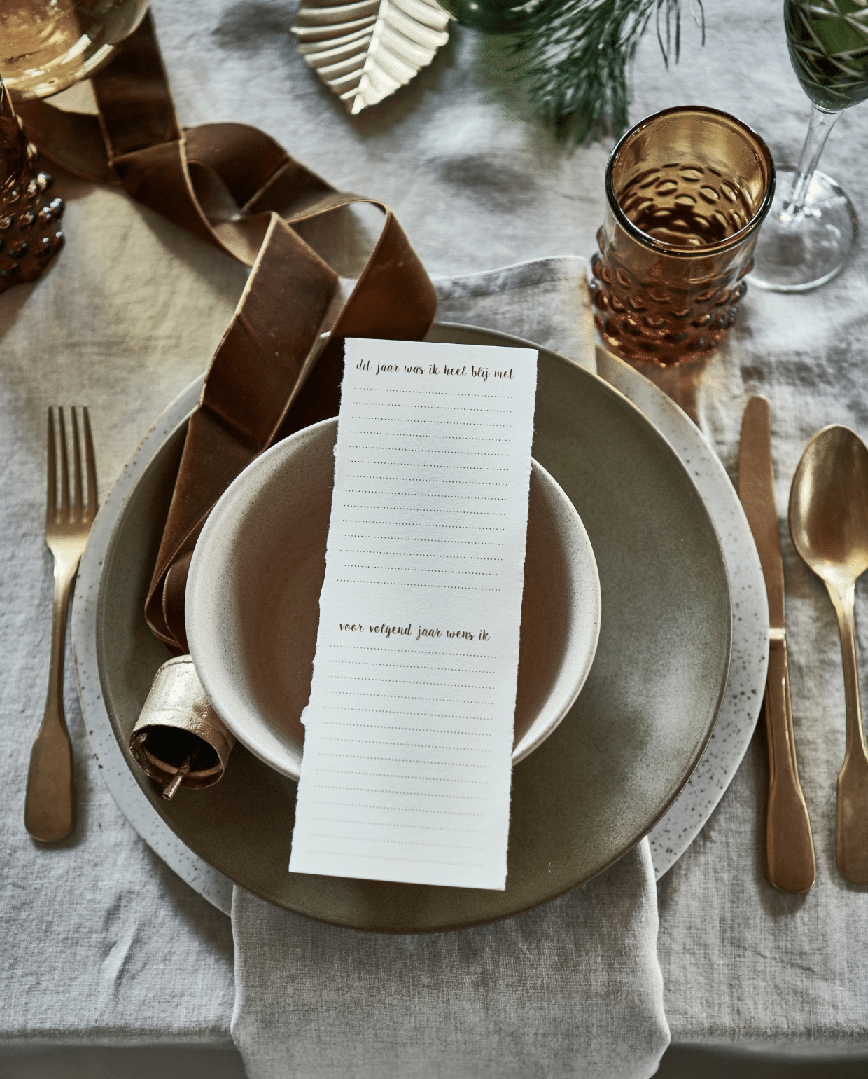 linnen tafelkleed € 39,99, servet, set van 2 € 9,99 (hm.com). Groen bord € 27,95, beige kom € xxxx, groen ovaal bord € xxx, alles aardewerk van Studio Ro Smit (factor-ij.amsterdam). Beige bord € 25,- (nordal.eu). Groen champagneglas, set van 6 € 160,- (polspotten.nl). Gouden kerstbal in vorm van bel, set van 2 € 15,-, gouden blad, set van 3 € 6,- (bungalow.dk). vtwonen 12-2021 | styling Danielle Verheul | Fotografie Sjoerd Eickmans | Tuin van Judith (groenstylist), assistentie Niels Kist, Kula van den Broek