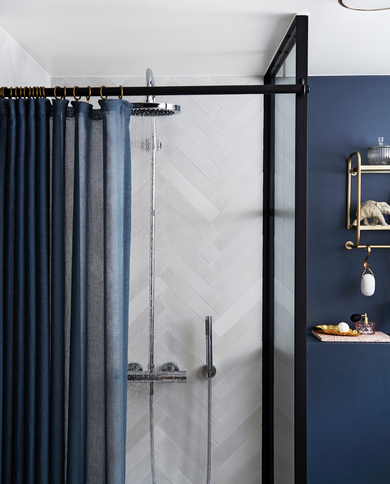 In de badkamer zorgen de Marokkaanse vloertegels, de matte donkerblauwe muren en messing details voor een behaaglijke wellness sfeer. Handgemaakte cementtegels Aztec Milk/Kohl, visgraat wandtegels Stix Fog, beide van Marokk. Het industriële glas is gemaakt door One Funky en Helstrand Smedje.