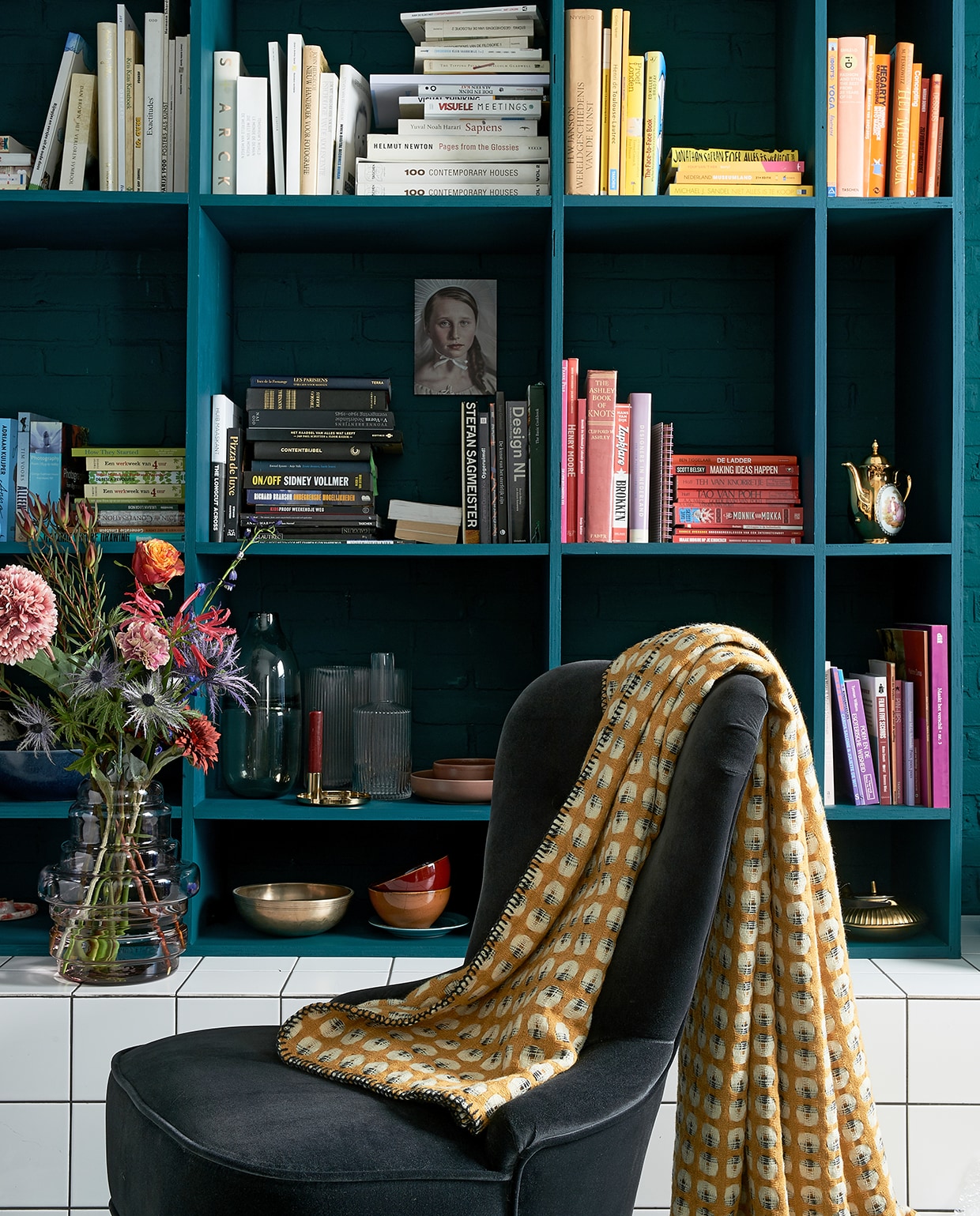 Boekenkast in kleur Marina Blue matte lak (Little Green). Fluwelen stoeltje Remsta (ikea.nl). Plaid Klara (made.com). Rood kommetje, mat gouden theepot. Grijze glazen vaas Rubygrey. Geribbelde vaas Hilmir, vaas Manfred. Kunstbloemen v.a.. Foto vrouw (racheldubbe.com). Overig privébezit.