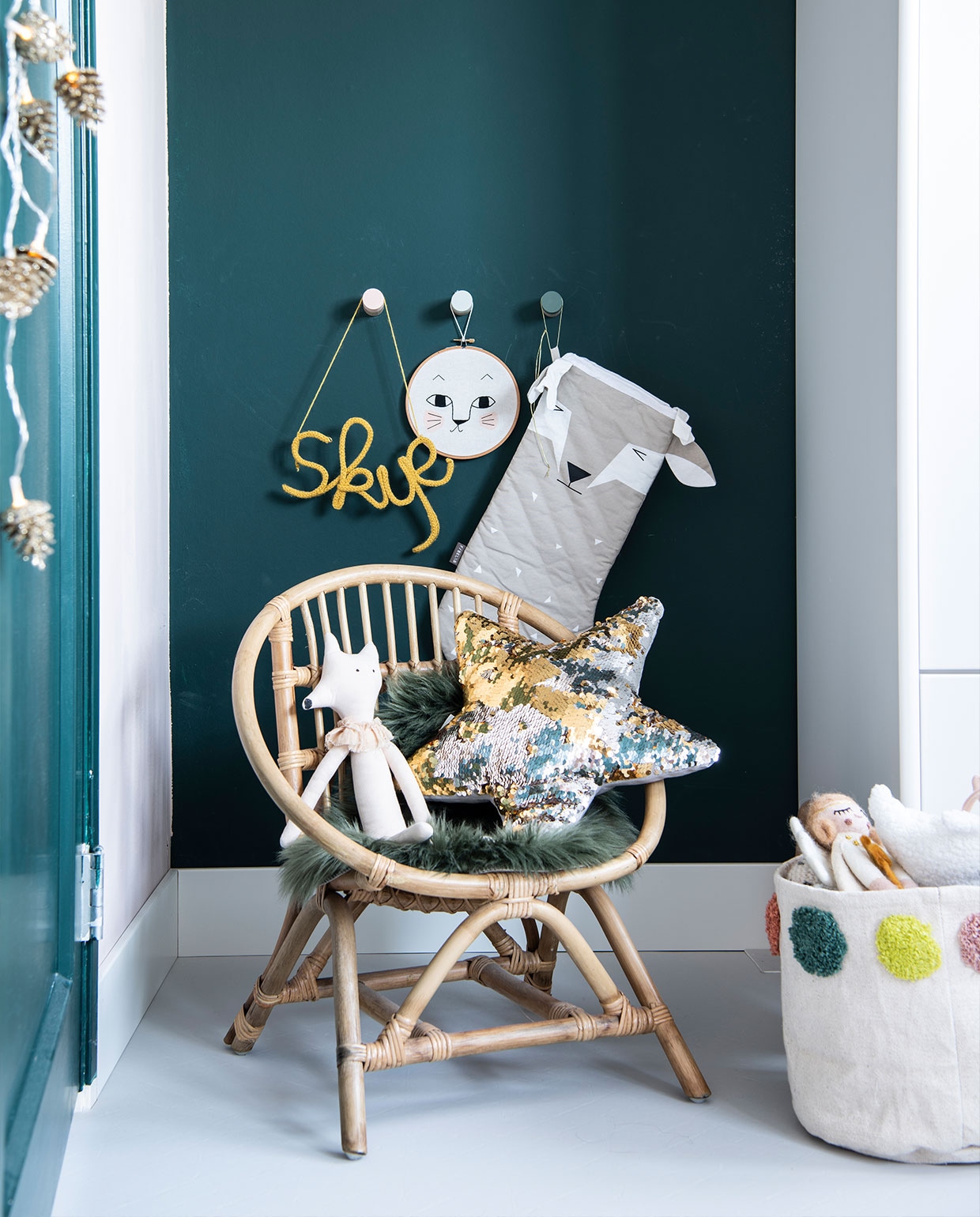 Stoel, groene placemat Casa. Ster-kussen H&amp;M Home. Pop Afkes. Opbergtas Hema. Guirlande van dennenappels Jysk. Wandhaken Kukeluusje. ‘Skye’ (naam geschreven met draad) jibbejebba.nl. Vloer Novilon. Overig herkomst onbekend.