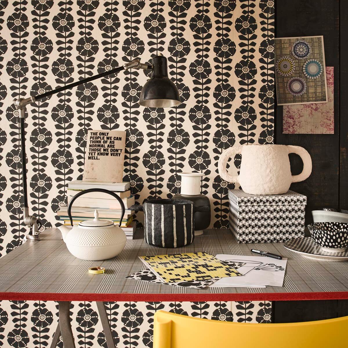Behang Black &amp; Light met grafische bloemenprint, tafelblad beplakt met behang Atlantic (Eijffinger). Gele kunststof stoel, schragen (Ikea). Zwarte bureaulamp (Neef Louis). Witte Japanse theepot, zwart-witte pot papier-maché, witte pot met oren, vaas zwart-wit, doos, bord, kom zwart-witte stip, beker met streep (Loods 5).