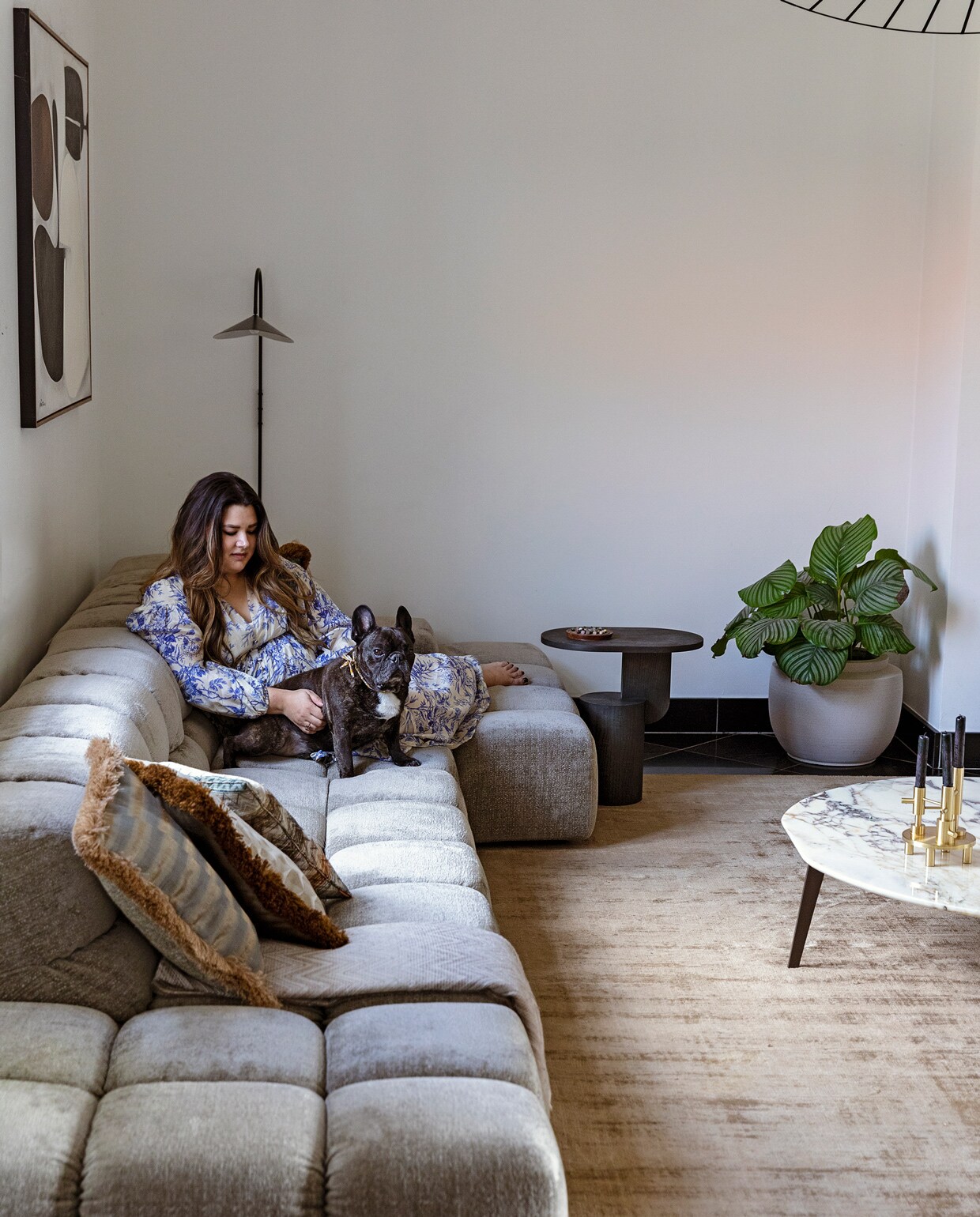 Vloerkleed Benuta. Marmeren bijzettafel Papadatos Decor Amsterdam. Kaarsenstandaard Fritz Hansen. Bank Tufty Time van BB Italia. Kussens Nox Studio Interiors en Missoni. Schilderij Ming Stylemeister. Wandlamp en zwarte bijzettafel Ferm Living. Plantenpot Serax. Plafondlamp Petite Friture via Interior Playground.