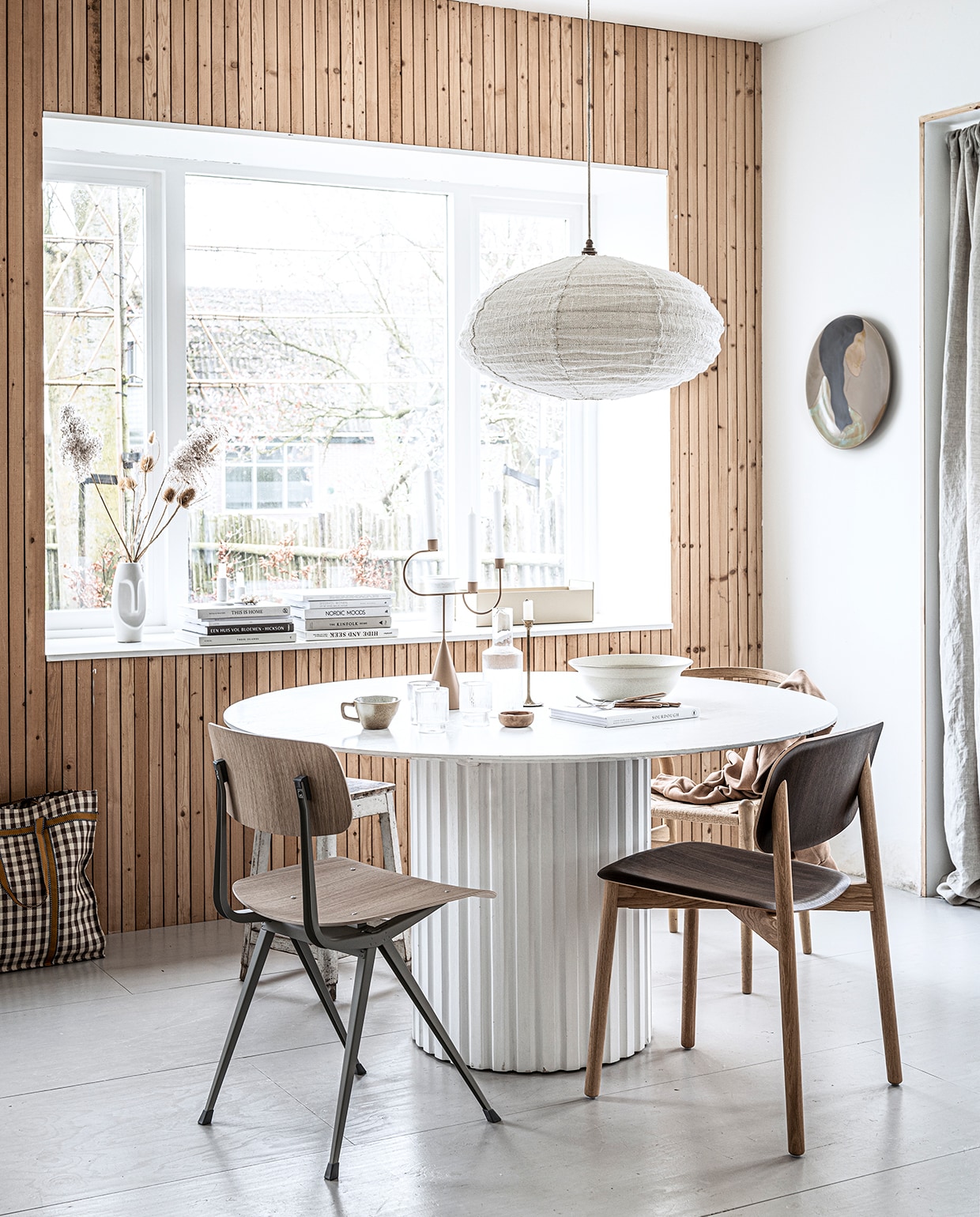 Eettafel Pillar van HKliving, 140×75 cm (Øxh), eetkamerstoel met stalen onderstel Result van Hay, geribbelde glazen van Ferm Living per 4, geribbelde karaf van Ferm Living, keramieken bord aan de wand Hessa van Ferm Living, beige kandelaar van Ferm Living, beige bak van Ferm Living (vtwonen.nl). Donker eikenhouten eetkamerstoel Hay Soft Edge, eikenhouten eetkamerstoel Wishbone CH24 (misterdesign.nl). Kookboek op tafel (hm.com). Stoffen hanglamp Kapok Tree in Natural/Beige (thebizzcollection.com). Linnen gordijn 140×300 cm, kopje, kom, houten bestek, shopper (zarahome.com). Overig privébezit.