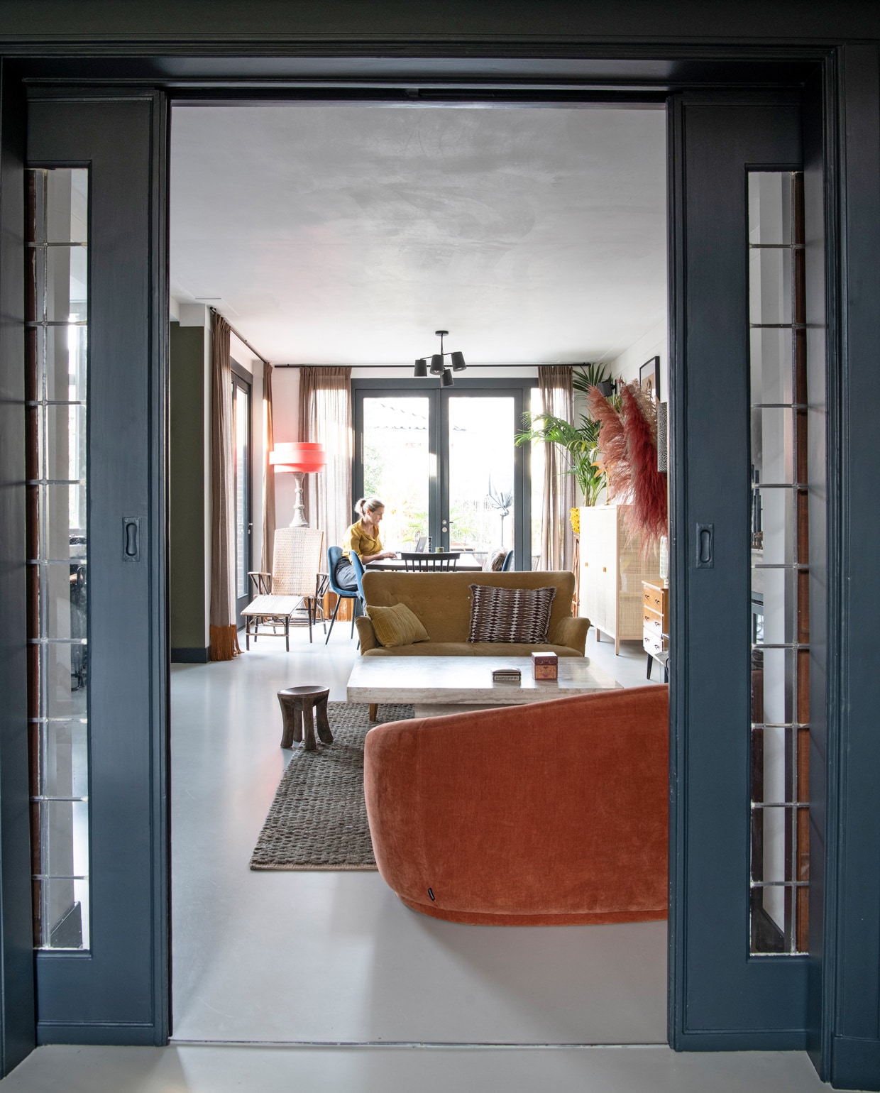 Blauwe verf op deuren Railings van Farrow &amp; Ball. Juten vloerkleed Crowd in Forest Green van Brinker Carpets. Kruk souvenir uit Tanzania. Gele bank Marktplaats, zelf bekleed. Marmeren salontafel Marktplaats. Oranje bank Sofacompany.com.