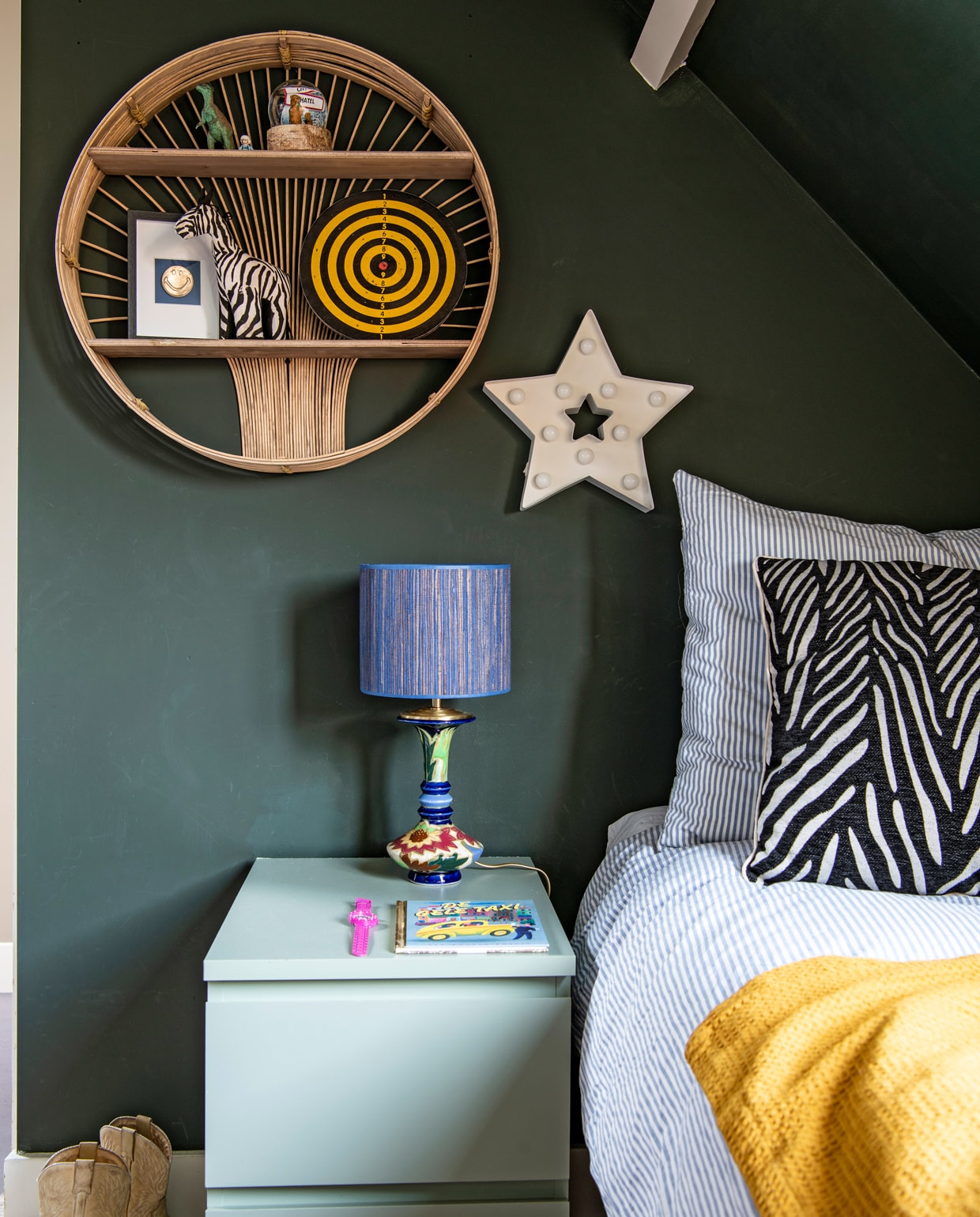Muurverf Studio Green van Farrow &amp; Ball. Rotan wandkastje Madam Stoltz. Sterrenlamp Hema. Nachtkastje en dekbedovertrek Ikea. Lamp Madame Garage. Kussen en plaid Kwantum.