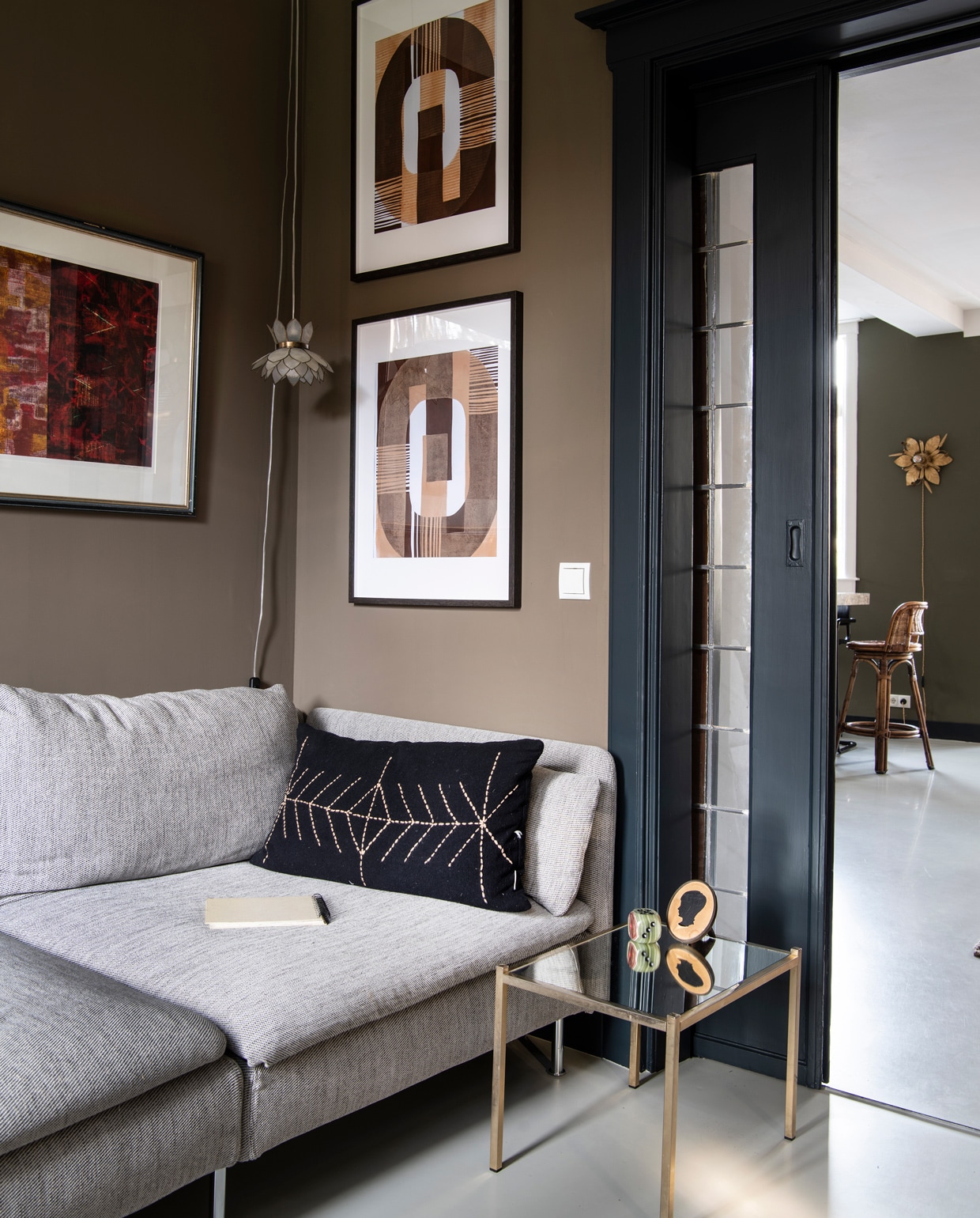 Muurverf Broccoli Brown van Farrow &amp; Ball. Kunstwerk links kringloop, rechts Enkel Art Studio. Bank Ikea, kussen Madam Stoltz. Bijzettafel kringloop, met zelf geplaatste spiegelplaat. Decoratiedobbelsteen en ingelijst portretje familiestuk. Hanglamp Marktplaats.