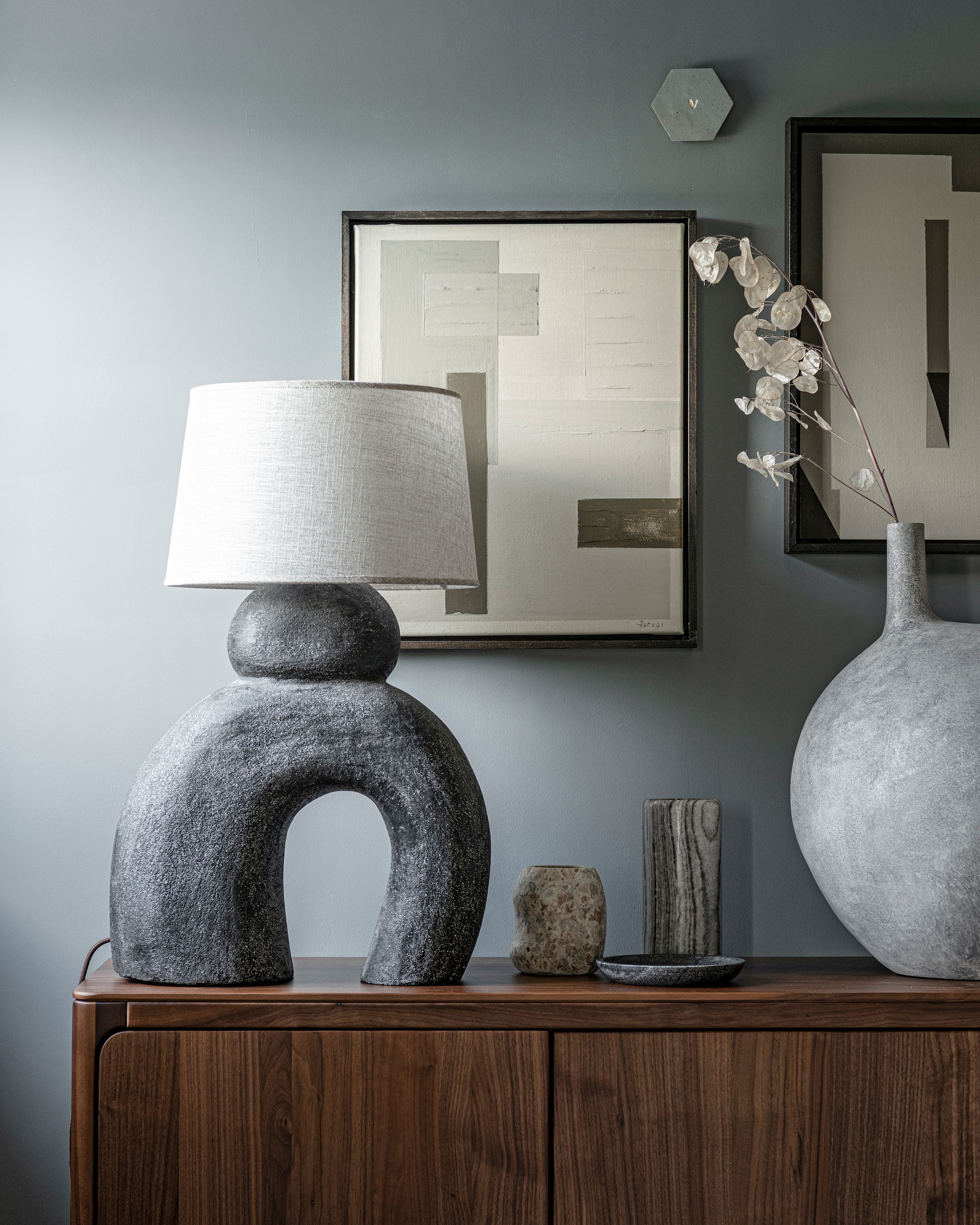 Kleur op wand Blue Stone van Pure &amp; Original 1 liter € 40,75 (pure-original). Lamp Sur € 449,95 (lanena-home.com). Kunstwerken, prijs op aanvraag (dailypat.com). Handgemaakte tegel met gegraveerd hart € 23,95 (tegeltjetegeltjeaandewand). Lichtgrijze vaas Submarine, big € 349,- (101cph.com). Marmeren vaas € 29,99 (hm.com). Stenen vaas € 45,99, stenen schaal € 22,99 (zarahome.com). Walnoothouten dressoir Rikke € 2960,- (demachinekamer).