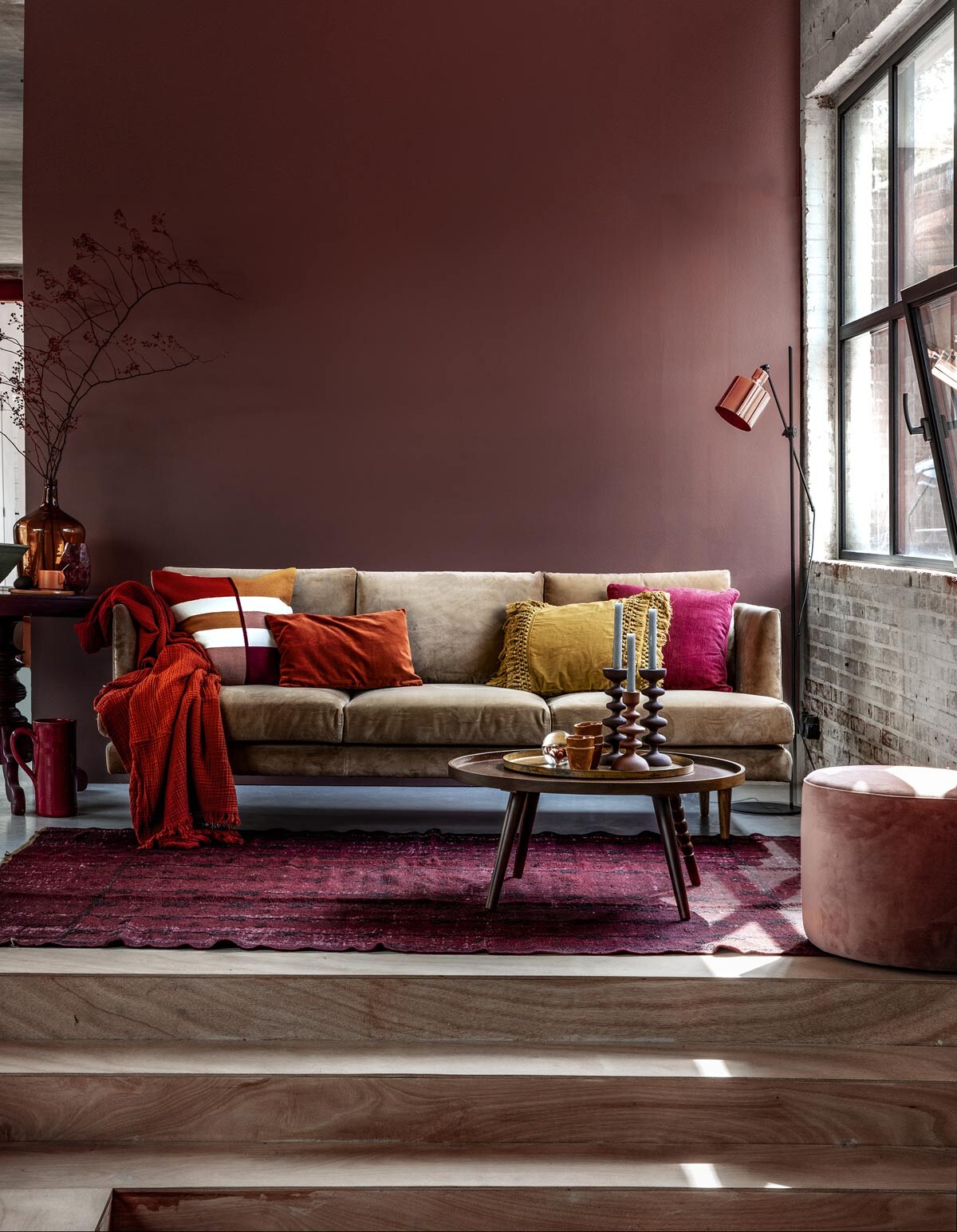 Muurverf Pure zijdemat Full Plum (Flexa). Beige velours 3-zitsbank Floyd, velours vintage Rosa poef (Sofacompany). Roestbruine crinkle plaid van HAY, vloerlamp Masterlight Industria 1020, okergeel kussen met franjes van Madam Stoltz (vtwonen.be). Kussen met gekleurde vlakken, roestbruin velours kussen, okergeel kopje, okergeel bord (H&amp;M Home). Donkerfuchsia kussen Milazzo Peony van Designers Guild (Wilhelmine van Aerssen). Wijnrode bijzettafel (Combitex). Donkergele flesvaas (Van Dijk &amp; Ko). Olijfgroene schaal, donkerrode kan (In-Petto). Vloerkleed (Ochre and Red). Salontafel Arabica van Dutchbone, kandelaars laag, hoog, presse-papier met bloem (Woondock). Roestbruine kopjes (Intratuin).