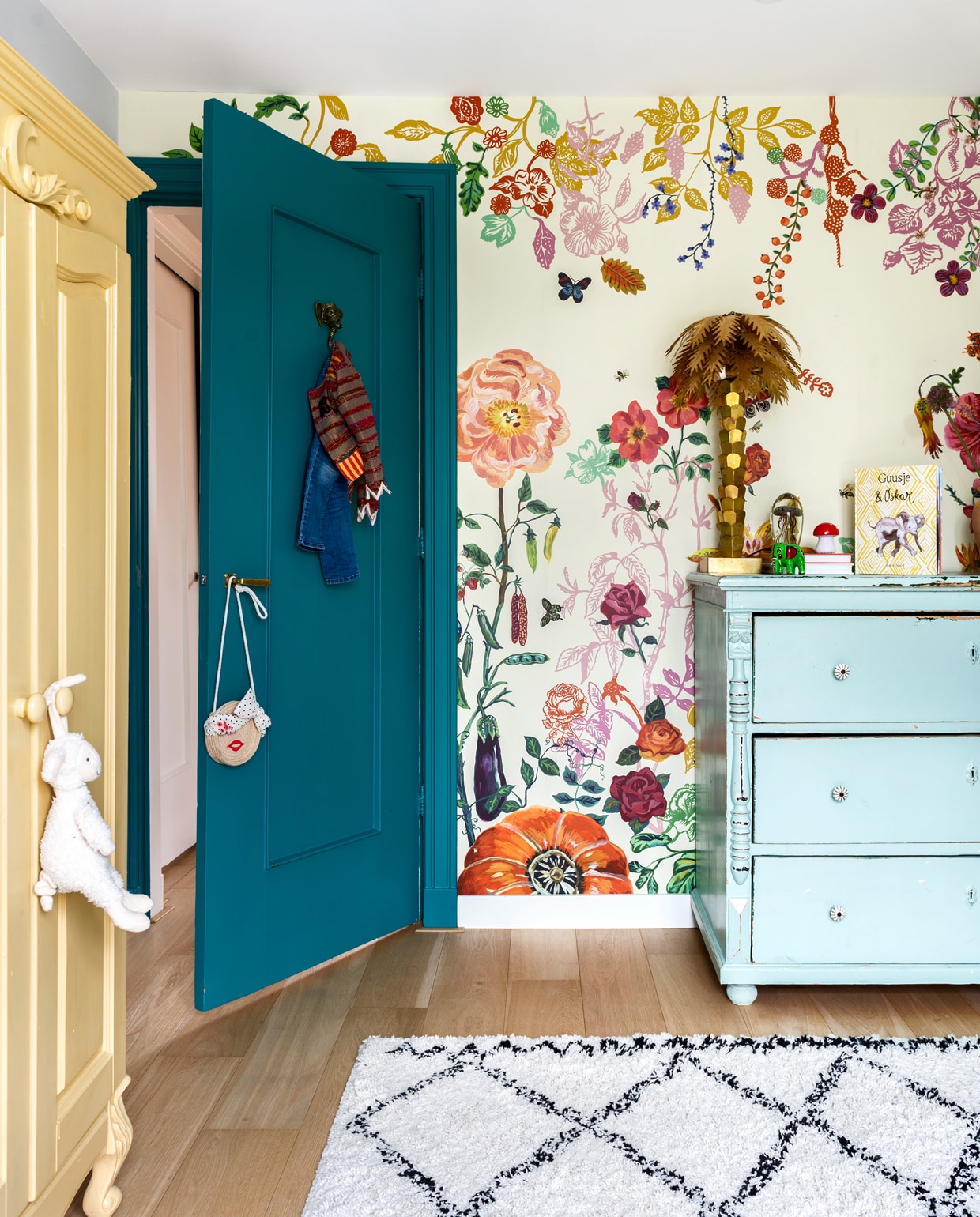 De kleurrijke kamer van Guusje. Behang van Nathalie Lété. Blauw kastje van Van Dijk en Ko. Palmboomlamp van HK Living. De gele kast stond al in het huis, Sophie verfde hem in Sudbury Yellow van Farrow &amp; Ball. Kleed Karwei. De deur is geschilderd in de kleur Vardo van Farrow &amp; Ball.